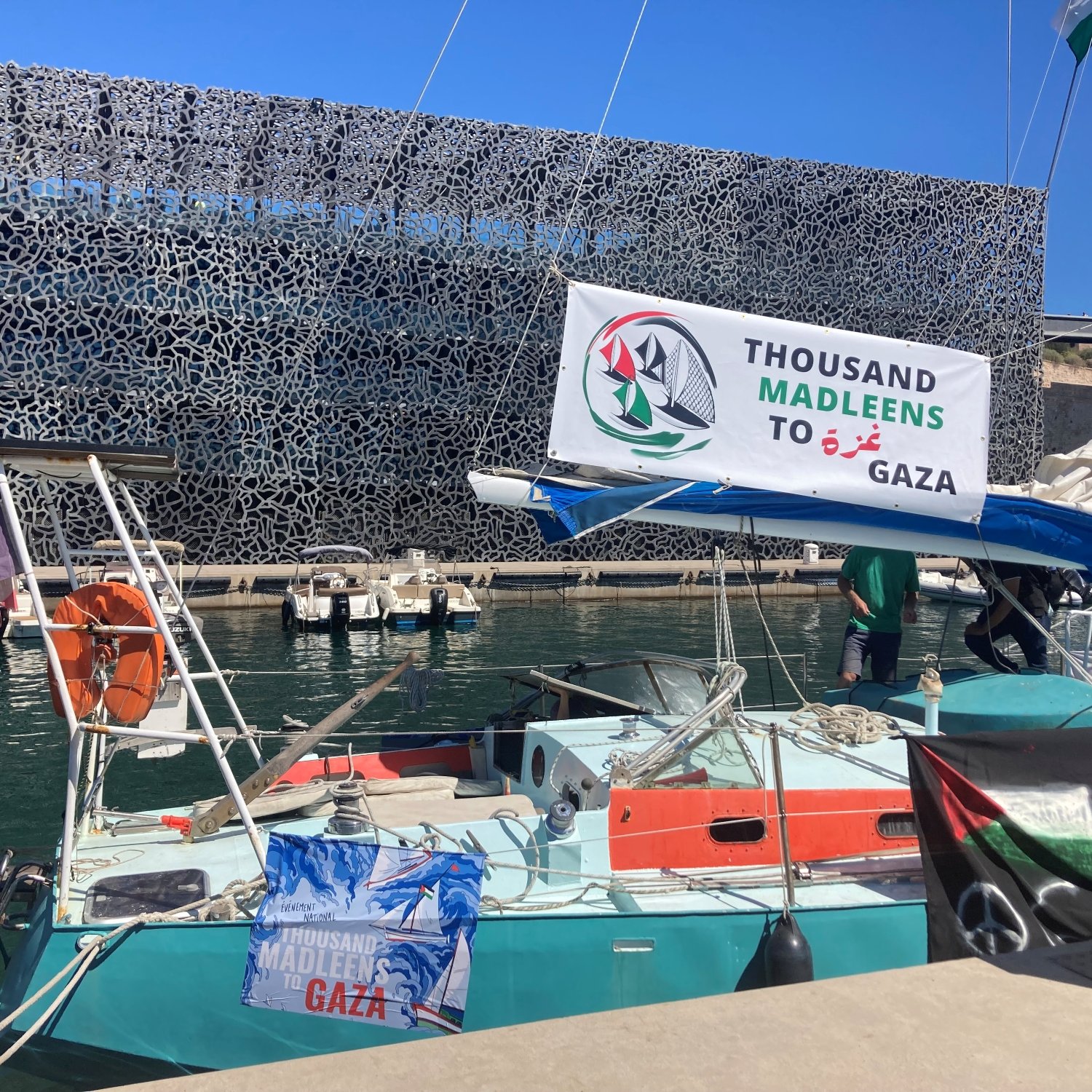 Un bateau avec une banderole "Thousand Madleen to Gaza" dans un port moderne.