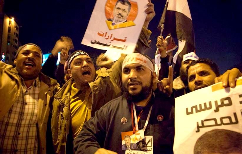 L'image montre un groupe de manifestants engagés dans une démonstration. Ils tiennent des pancartes et des drapeaux, exprimant visiblement leurs opinions politiques. Les visages des participants montrent des émotions intenses, allant de la passion à la détermination. Les slogans et les portraits visibles sur les affiches semblent se rapporter à un leader ou une figure politique, témoignent d'un moment de mobilisation collective. L'ambiance est dynamique, évoquant un fort sentiment de communauté et d'engagement.