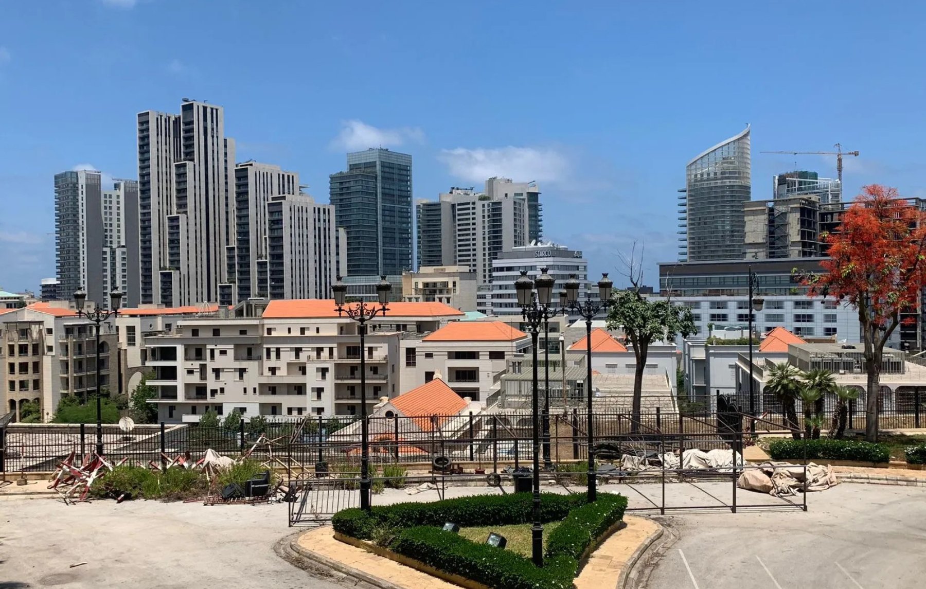 صورة لمدينة حديثة، مباني مرتفعة، سماء زرقاء وأشجار. يبدو النشاط العمراني واضحًا.