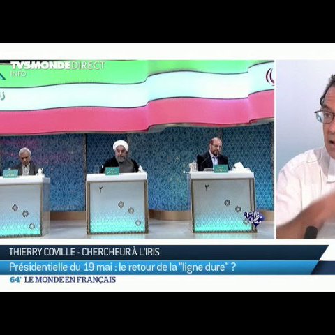 L'image présente une scène de débat ou de discussion, probablement liée à la politique. Au centre de l'image, on voit Thierry Coville, chercheur à l'IRIS, qui s'exprime avec des gestes. Derrière lui, trois personnes sont assises, dont l'une porte un costume clair. Le contexte semble lié à une élection présidentielle, évoquant des thèmes tels que la "ligne dure". L'image reflète un moment d'échange d'idées sur des enjeux politiques.