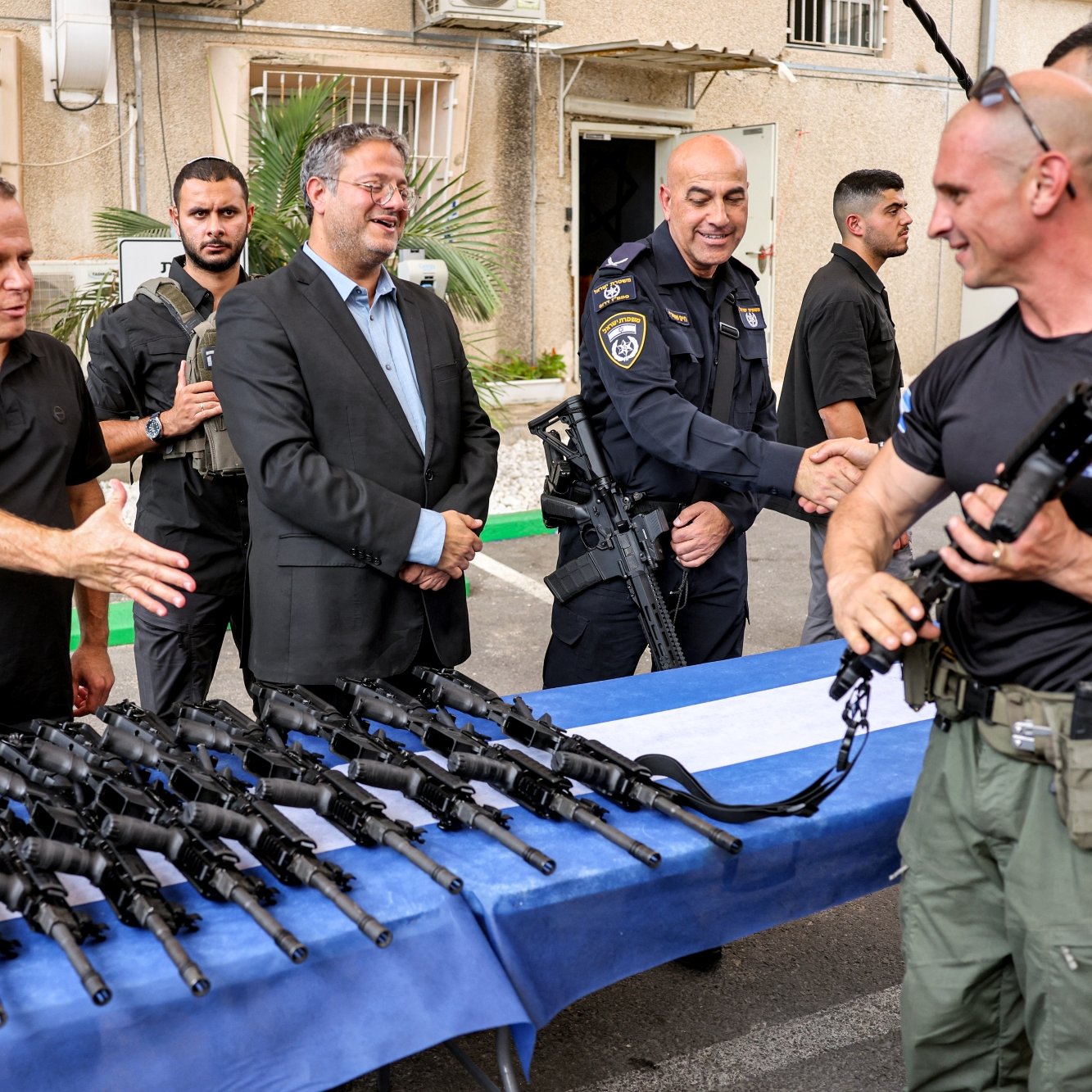 Des hommes en uniforme échangent des armes sur une table, sourires et discussions.