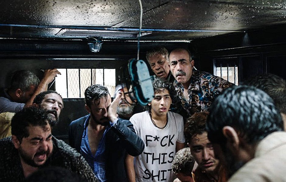 الصورة تظهر مجموعة من الأشخاص الذين يتواجدون في مكان مغلق، يبدو عليهم الارتباك والقلق. هناك مظاهر للفوضى، حيث يظهر بعضهم بمظهر متعب أو مضغوط. الإضاءة في المكان ضعيفة، مما يضيف شعورًا بالتوتر. يبدو أن الوضع في الصورة يعكس حالة صعبة أو حرجة.