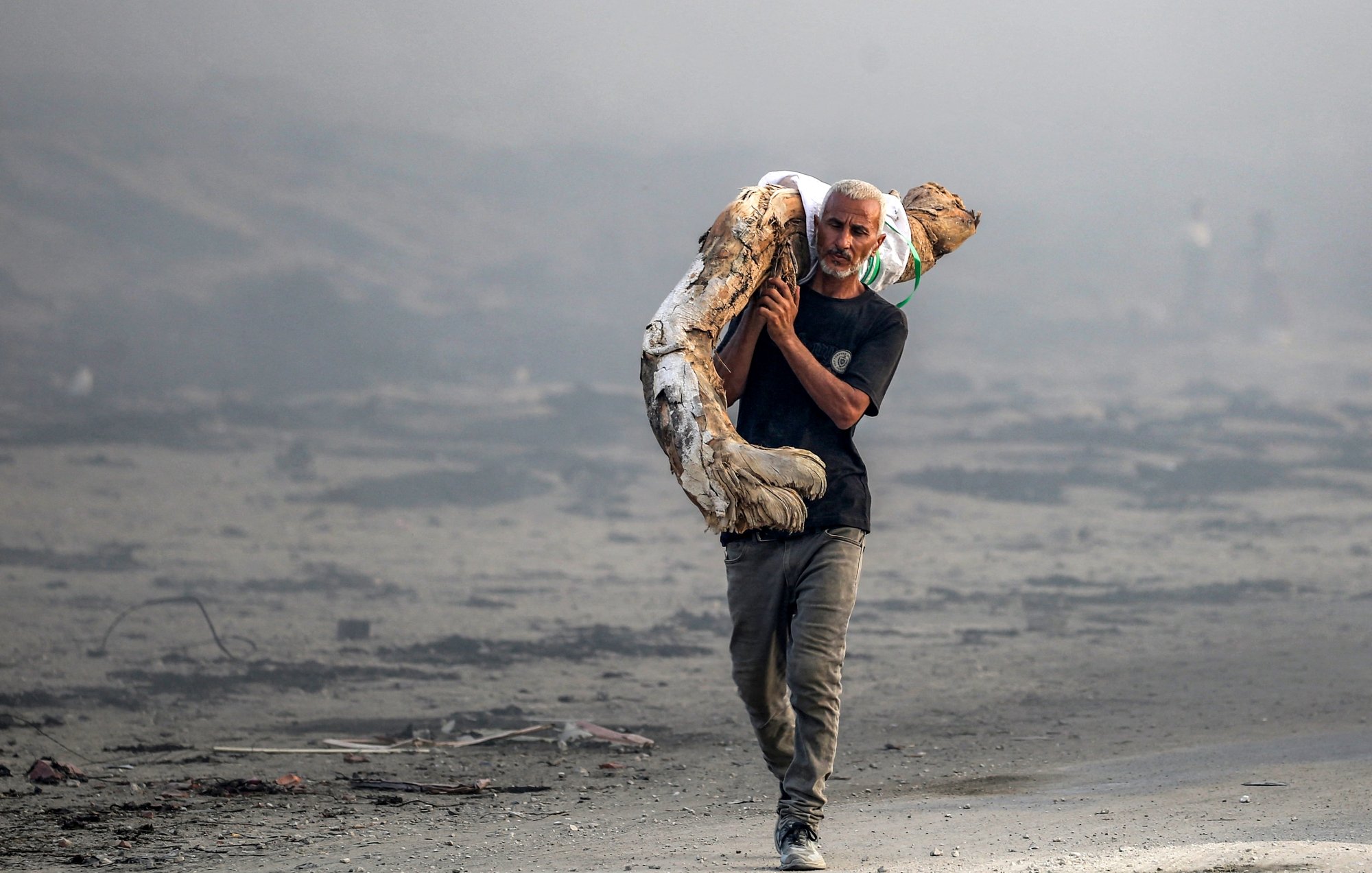 Un uomo attraversa un paesaggio desolato, portando un oggetto pesante sulle spalle.