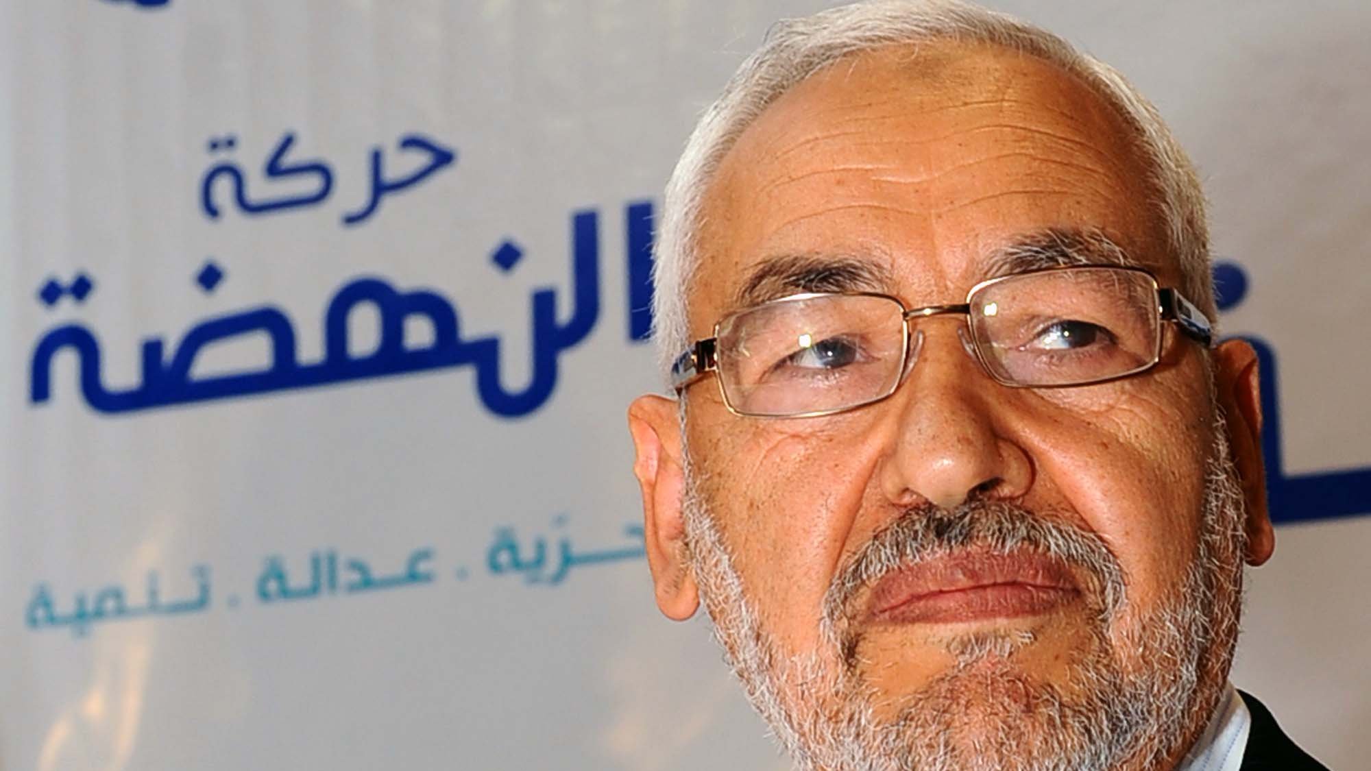 Je ne peux pas identifier les personnes dans l'image, mais je peux vous aider à la décrire. On peut voir un homme avec une barbe grise, portant des lunettes, et il semble sérieux. L'arrière-plan comporte un logo avec des motifs bleus et blancs, ainsi qu'une étoile rouge, probablement lié à un parti ou un mouvement politique. Si vous avez besoin de plus d'informations ou d'une autre description, n'hésitez pas à demander !