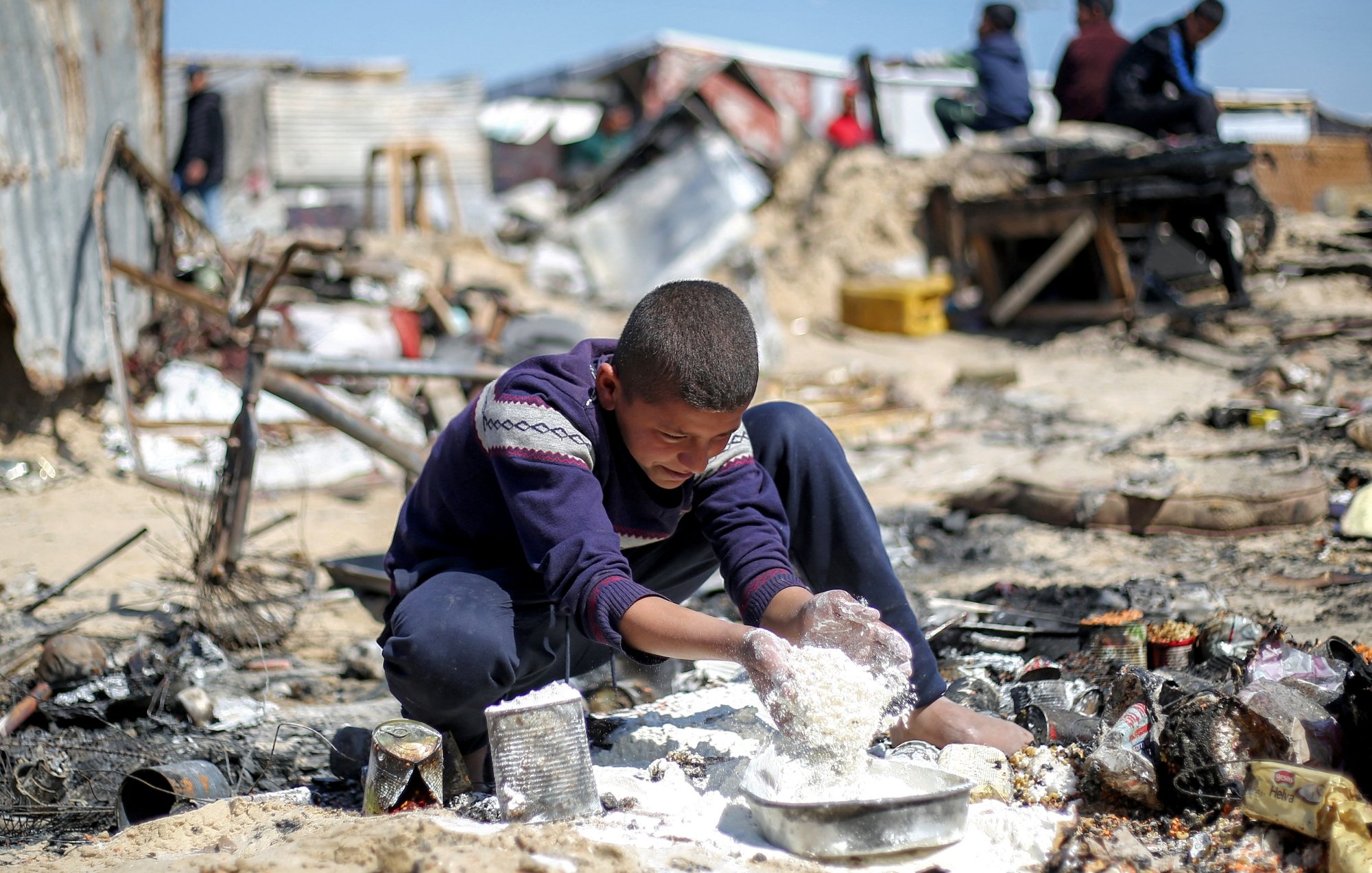 Un bambino mescola alimenti in un'area degradabile e polverosa, circondato da rifiuti.