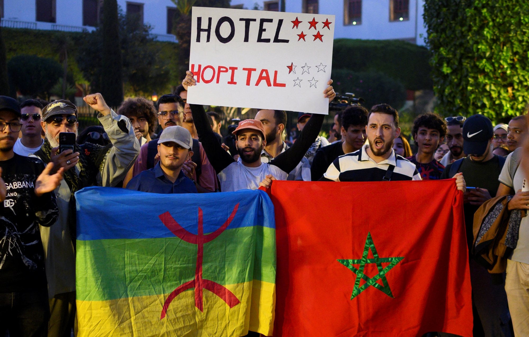 Manifestation avec des drapeaux marocains et amazigh, pancarte pour un hôtel.