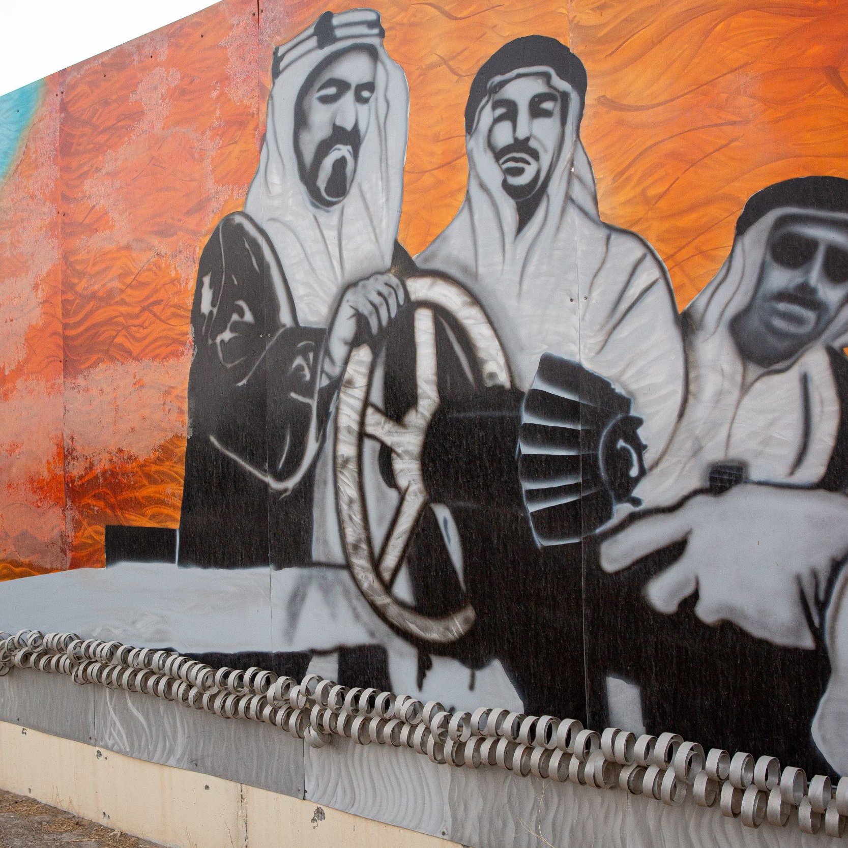 L'image représente une grande fresque murale. On y voit des figures en vêtements traditionnels arabes, probablement des hommes, qui semblent interagir avec des éléments symboliques liés à l'industrie pétrolière. L'arrière-plan est composé de couleurs vives, notamment des nuances de bleu et d'orange. Cette œuvre évoque des thèmes de culture, de tradition et de développement industriel, sur fond de paysages désertiques. La composition suggère un sens de la coopération et de l'engagement vers une vision commune.
