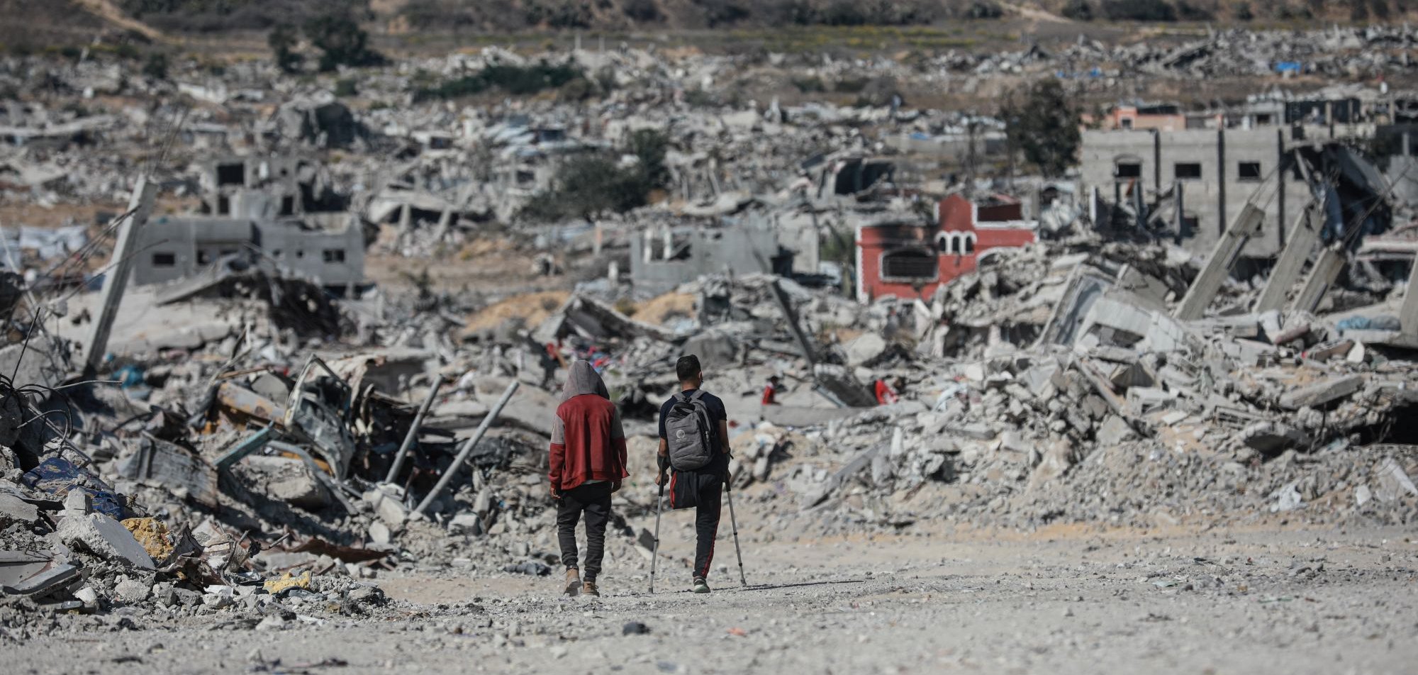 Deux personnes marchent dans un paysage de destruction, entourées de débris.