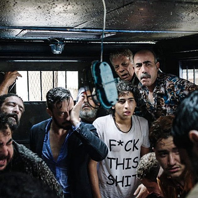 الصورة تظهر مجموعة من الأشخاص الذين يتواجدون في مكان مغلق، يبدو عليهم الارتباك والقلق. هناك مظاهر للفوضى، حيث يظهر بعضهم بمظهر متعب أو مضغوط. الإضاءة في المكان ضعيفة، مما يضيف شعورًا بالتوتر. يبدو أن الوضع في الصورة يعكس حالة صعبة أو حرجة.