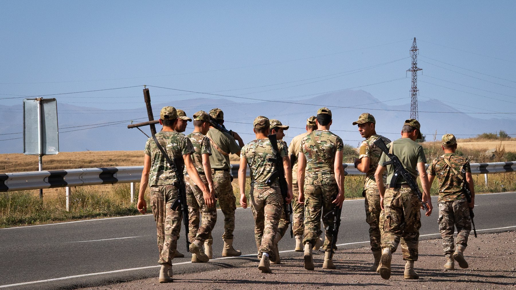 Des soldats marchent en groupe sur une route, avec des montagnes en arrière-plan.