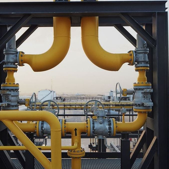 الصورة تظهر نظام أنابيب صناعي مركب، حيث تتداخل أنابيب ملونة باللون الأصفر مع بعض العناصر المعدنية. تُظهر الأنابيب مجمعًا من الصمامات والتجهيزات المستخدمة في نقل السوائل أو الغاز، ويمكن رؤية جزء من المنشأة الصناعية في الخلفية. الأجواء المحيطة تبدو هادئة وتدل على موقع صناعي حيث يتم التعامل مع مواد متنوعة.