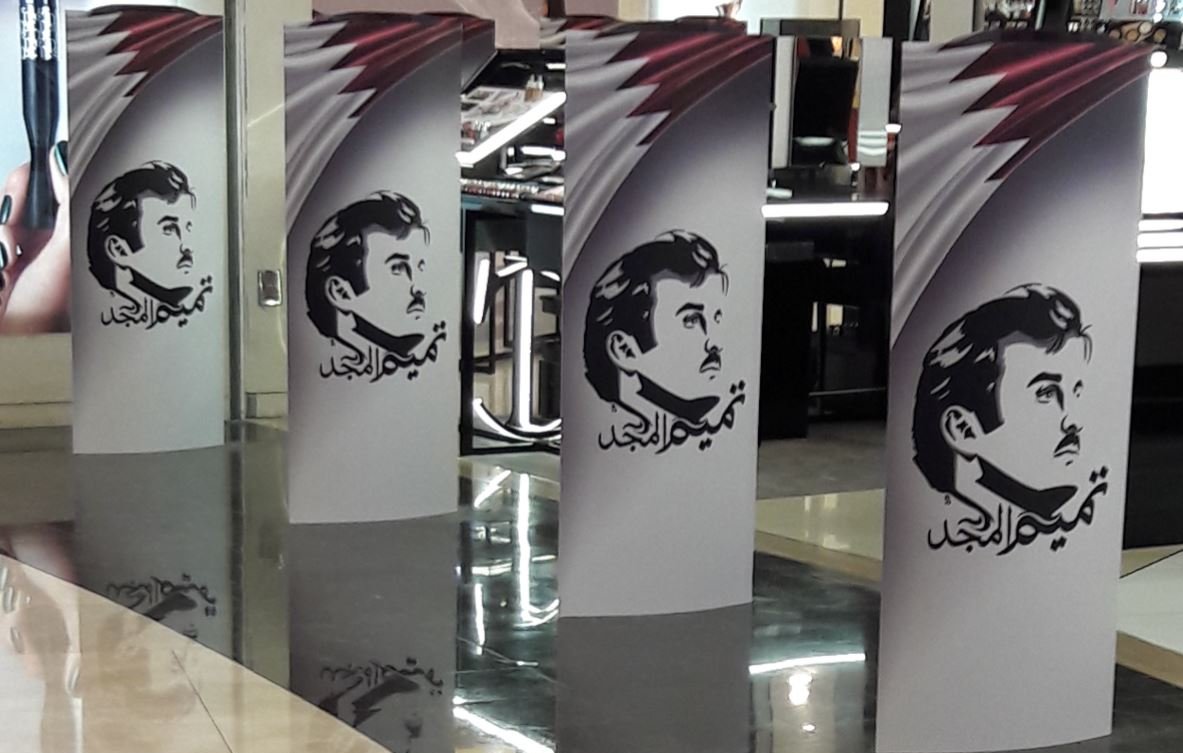 L'image montre plusieurs panneaux verticaux disposés en ligne. Chaque panneau présente un motif similaire, avec un fond qui semble afficher des couleurs en dégradé, accompagnés d'une illustration d'un homme avec une moustache. Sur les panneaux, on peut également observer des éléments de texte en arabe. L'ensemble donne une impression moderne et artistique, probablement lié à un événement ou une exposition.