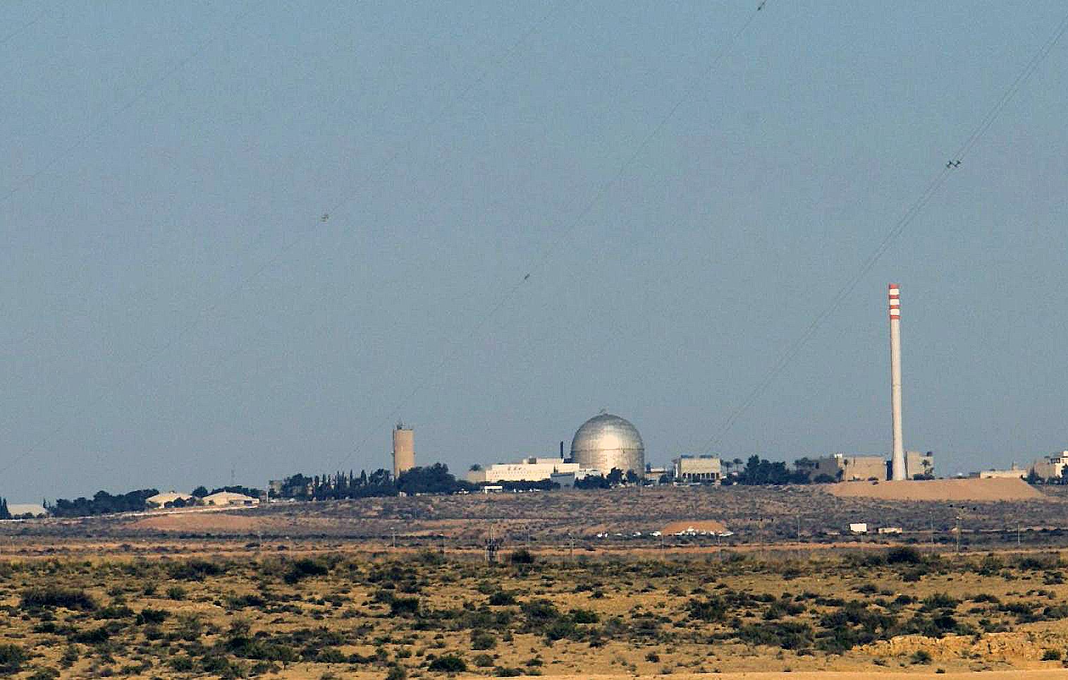 الصورة تظهر مشهداً لبيئة طبيعية صحراوية مع مبانٍ تظهر في الخلفية. يبدو أن هناك مرفقاً يحتوي على قبة كبيرة، ومن المحتمل أن يكون هذا المرفق مركزاً علمياً أو مفاعلاً نووياً. كما يُلاحظ وجود أعمدة مدخنة تشير إلى أنشطة صناعية. السماء صافية واللون العام للصورة يميل إلى الألوان الترابية.