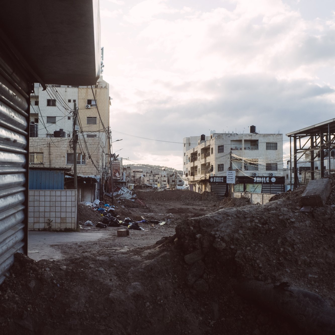 Vue d'une rue déserte avec des bâtiments et des gravats, ciel nuageux en arrière-plan.