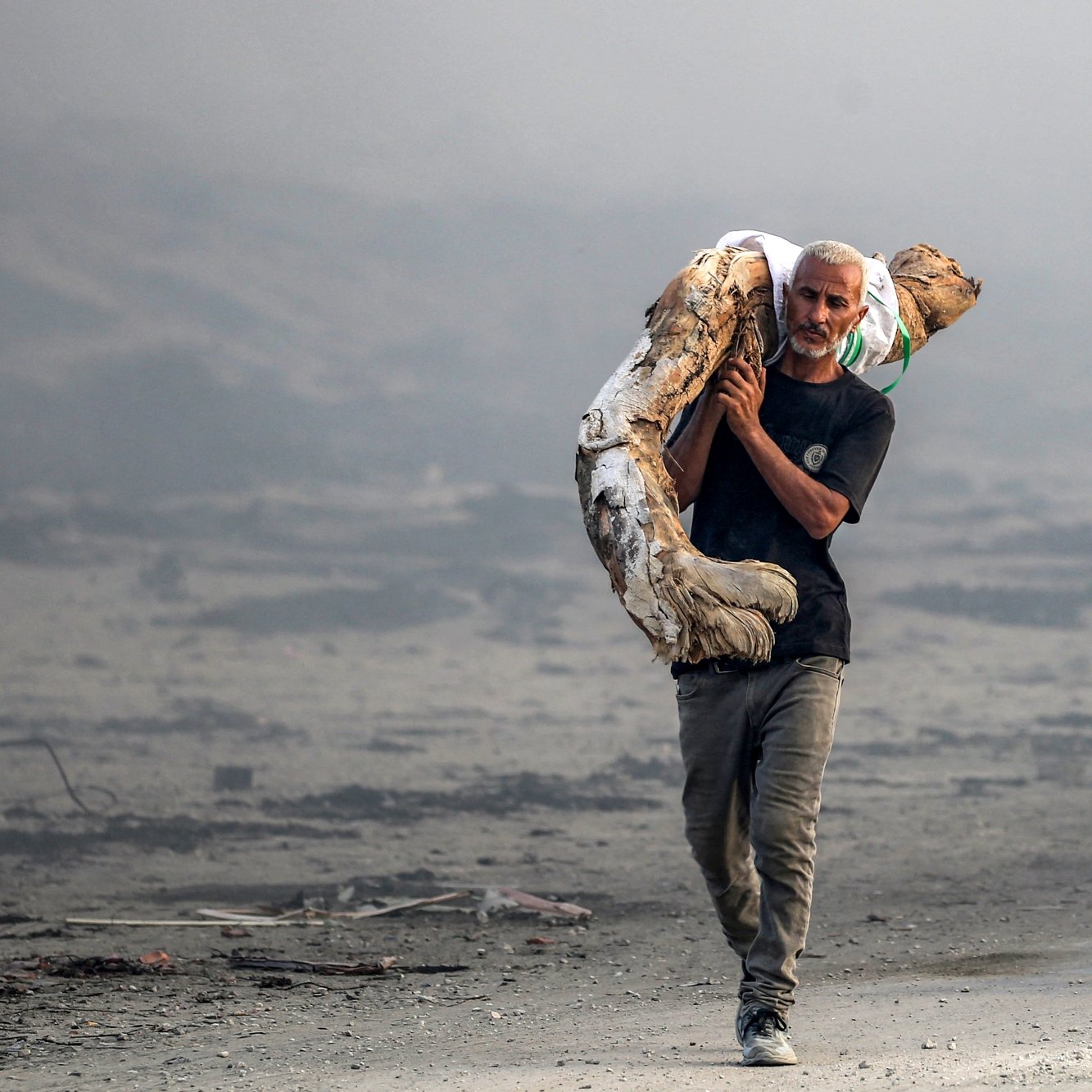Un uomo attraversa un paesaggio desolato, portando un oggetto pesante sulle spalle.