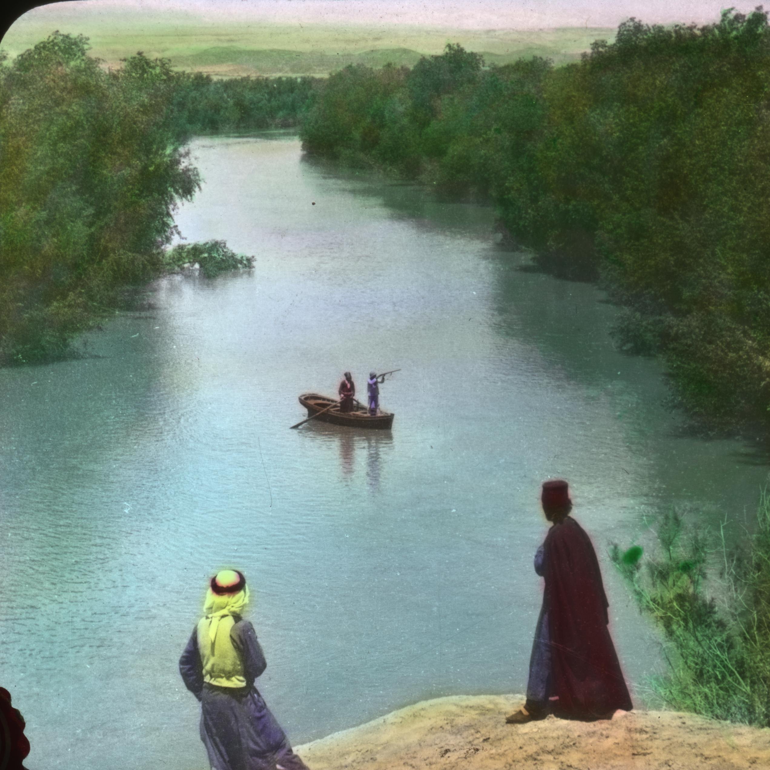 L'image montre une scène paisible au bord d'une rivière. Deux personnes se tiennent sur la berge, regardant une barque qui navigue sur l'eau. La barque semble être occupée par deux personnes qui sont en train de pêcher ou d'observer les environs. La végétation entourant la rivière est dense et verdoyante, ajoutant une touche de nature à la scène. Le ciel est clair et dégage une atmosphère calme et sereine.