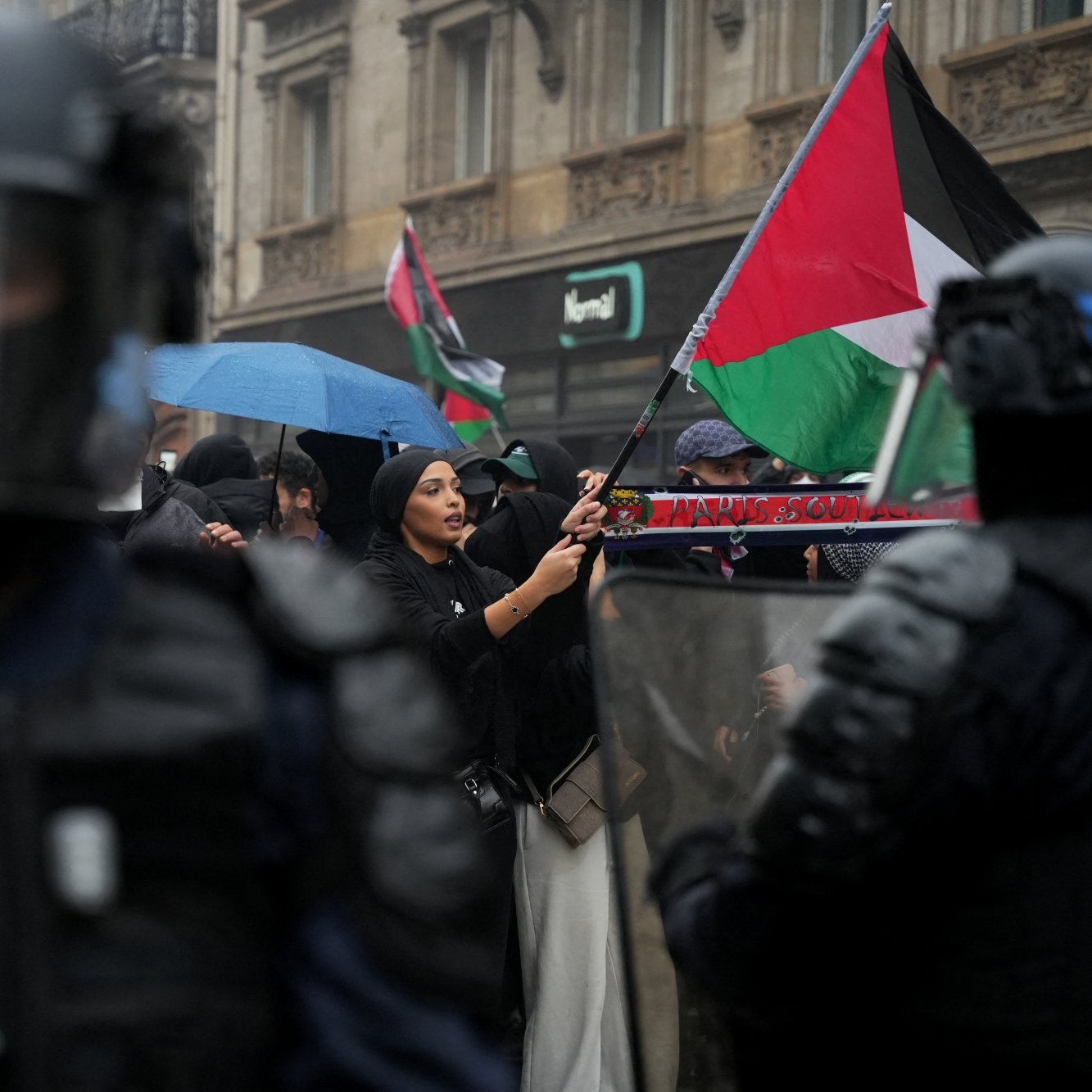 Manifestation avec des drapeaux palestiniens, policiers en tenue anti-émeute, ambiance tendue.