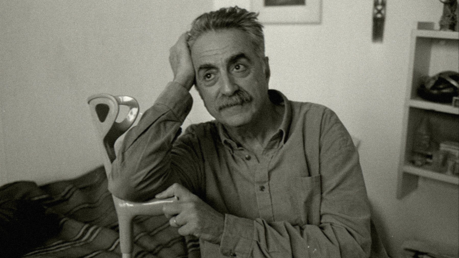 Homme pensif, assis, avec une canne, dans une pièce simple et lumineuse.