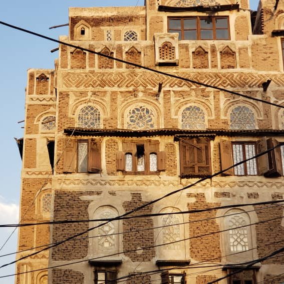 الصورة تُظهر مباني قديمة مزخرفة بشدة، مع مئذنة عالية وخطوط كهربائية متقاطعة.