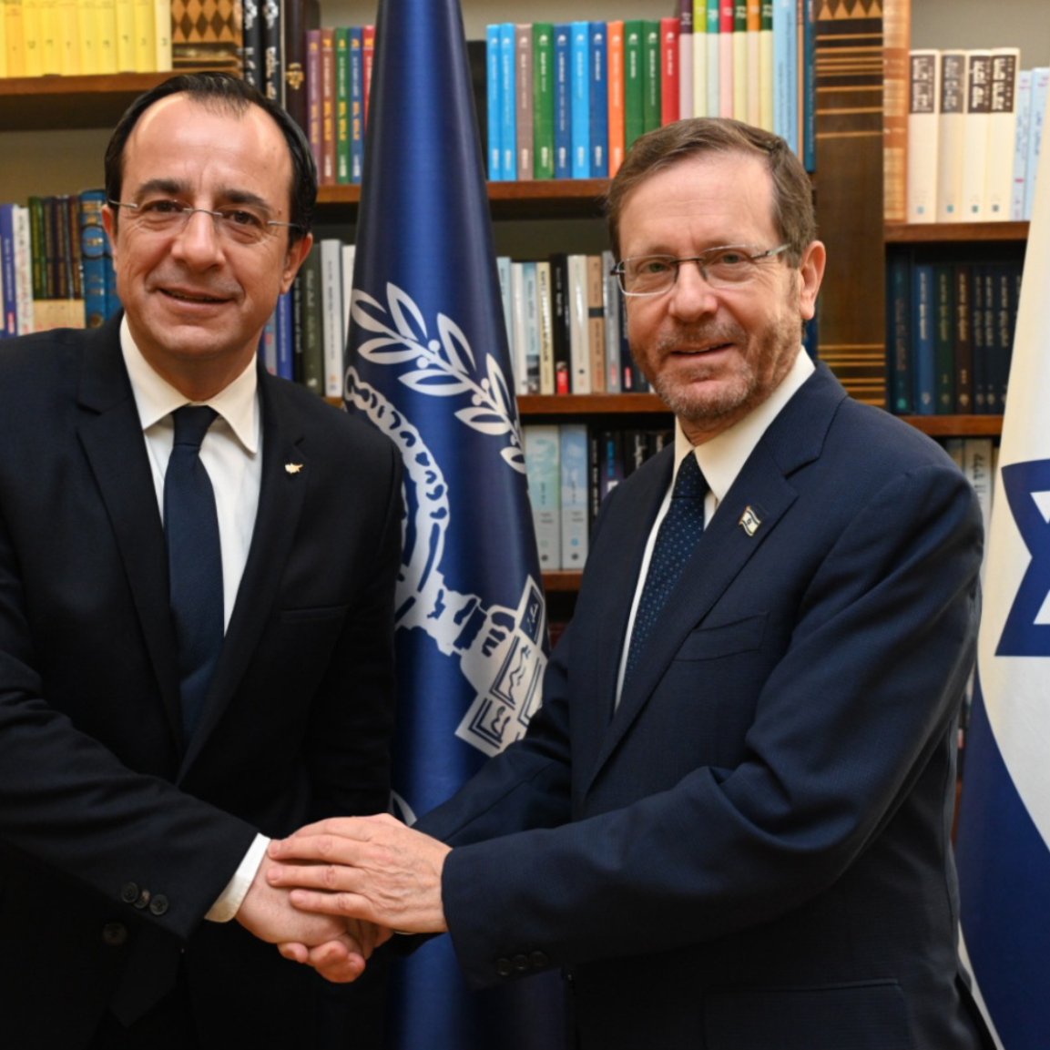 دو مرد در یک کتابخانه دست هم را گرفته‌اند. پرچم‌های قبرس و اسرائیل در پس‌زمینه هستند.