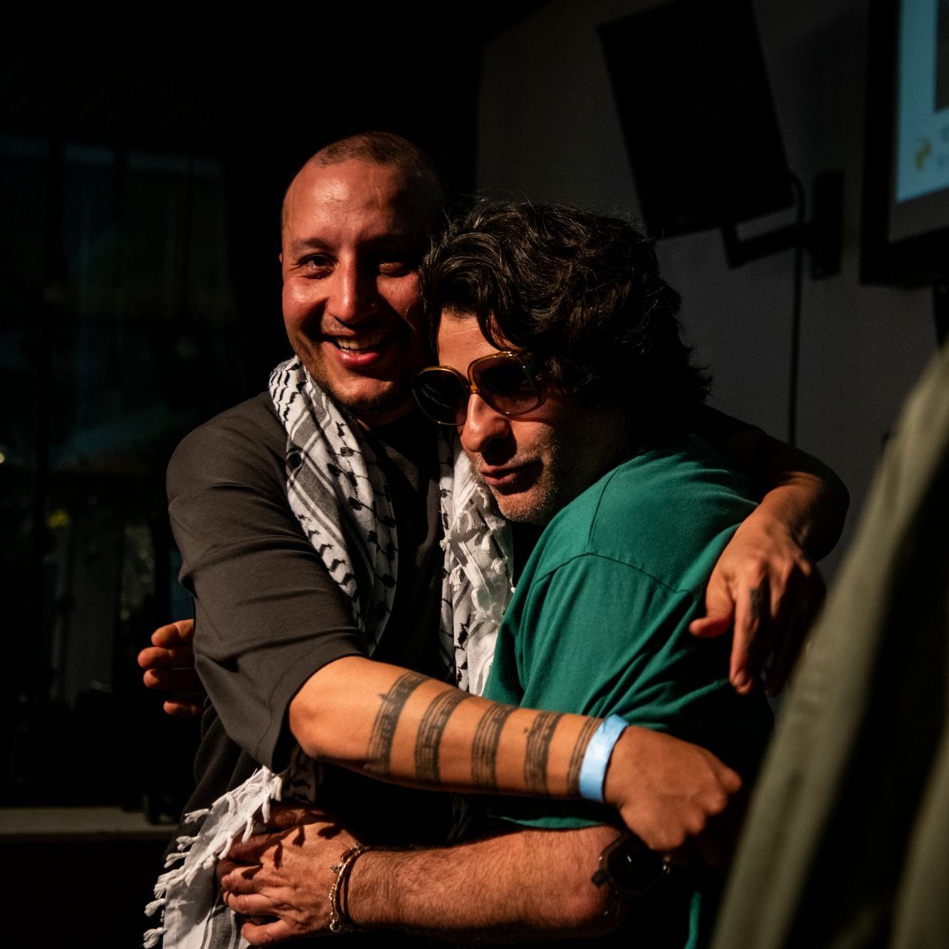 Deux hommes s'étreignent, souriants, avec des déguisements et un ambiance chaleureuse.