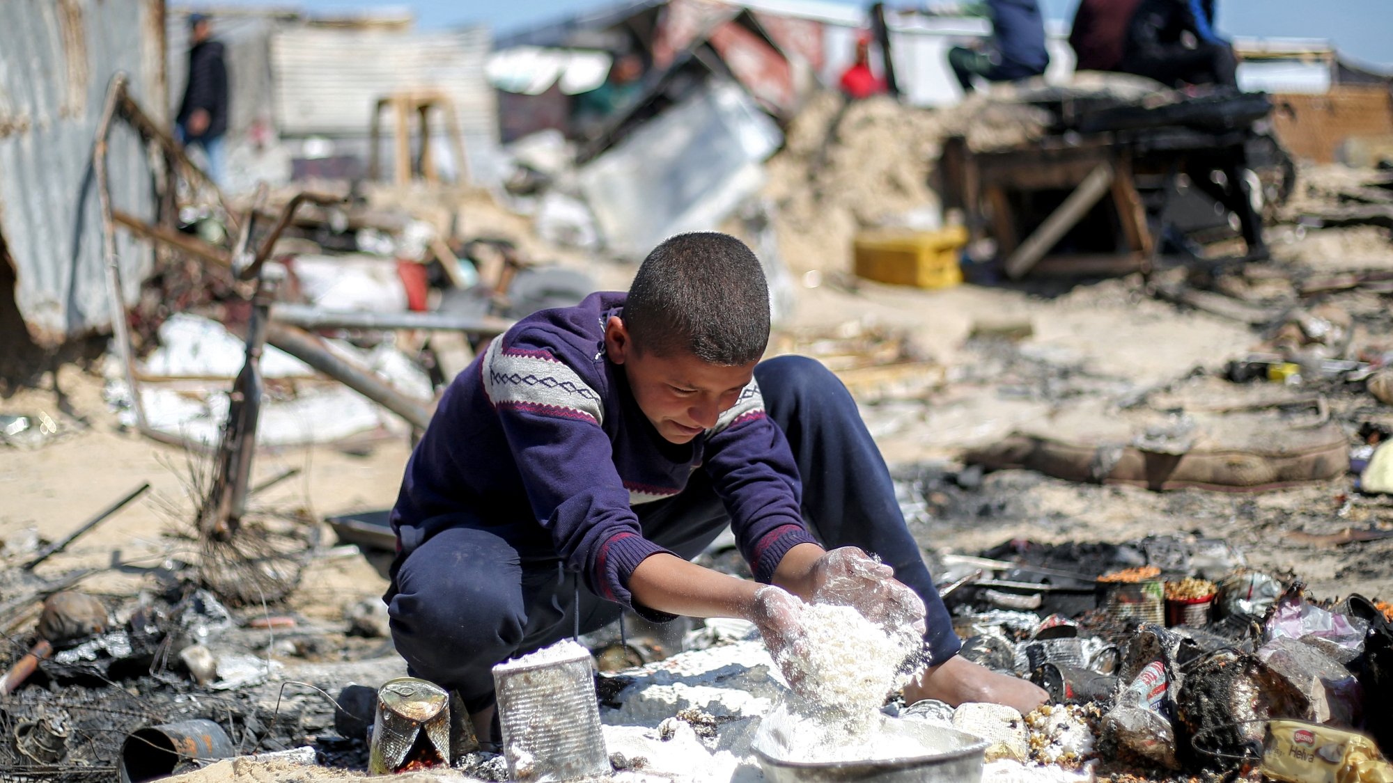 Un bambino mescola alimenti in un'area degradabile e polverosa, circondato da rifiuti.