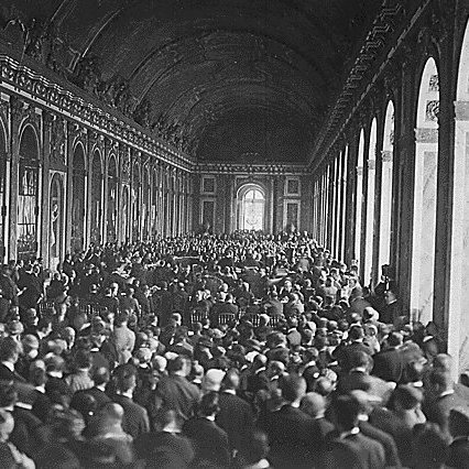 L'image montre une vaste salle intérieure, probablement un palais, remplie d'un grand nombre de personnes. On peut voir des rangées de chaises disposées, et les murs sont ornés de grandes fenêtres et de détails architecturaux. La foule semble rassemblée pour un événement ou une cérémonie importante, créant une atmosphère dense et dynamique dans cet espace majestueux. La lumière pénètre par les fenêtres, ajoutant une ambiance solennelle à la scène.