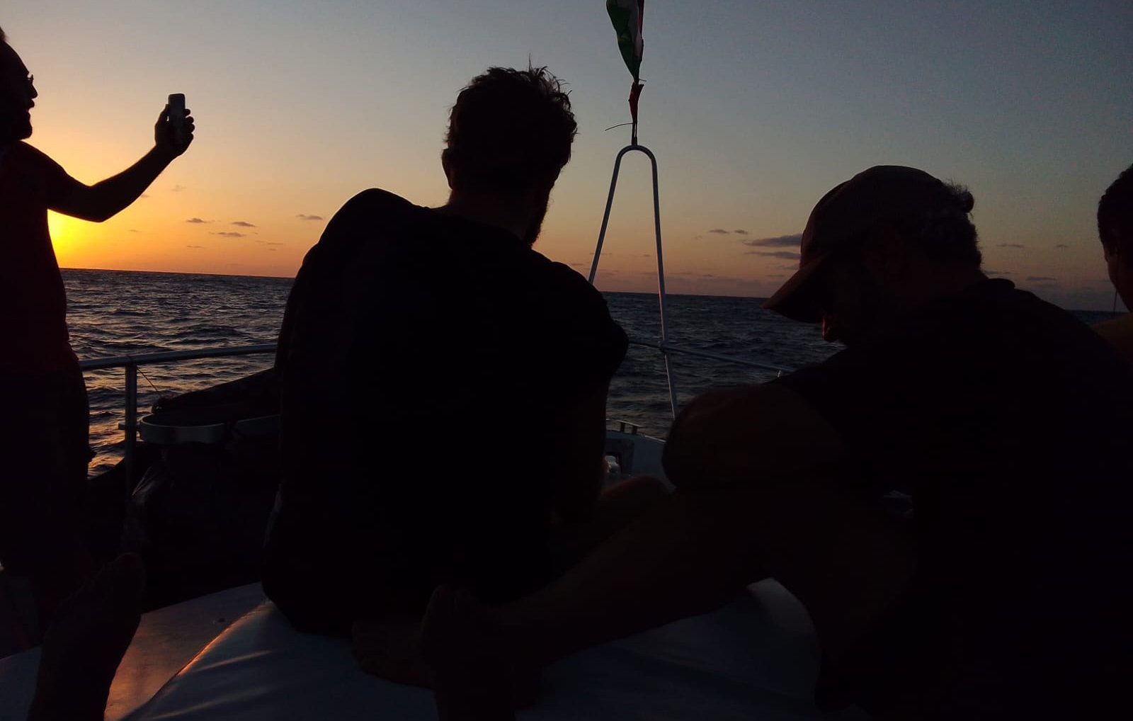 Silhouettes de personnes sur un bateau au coucher du soleil, mer calme.