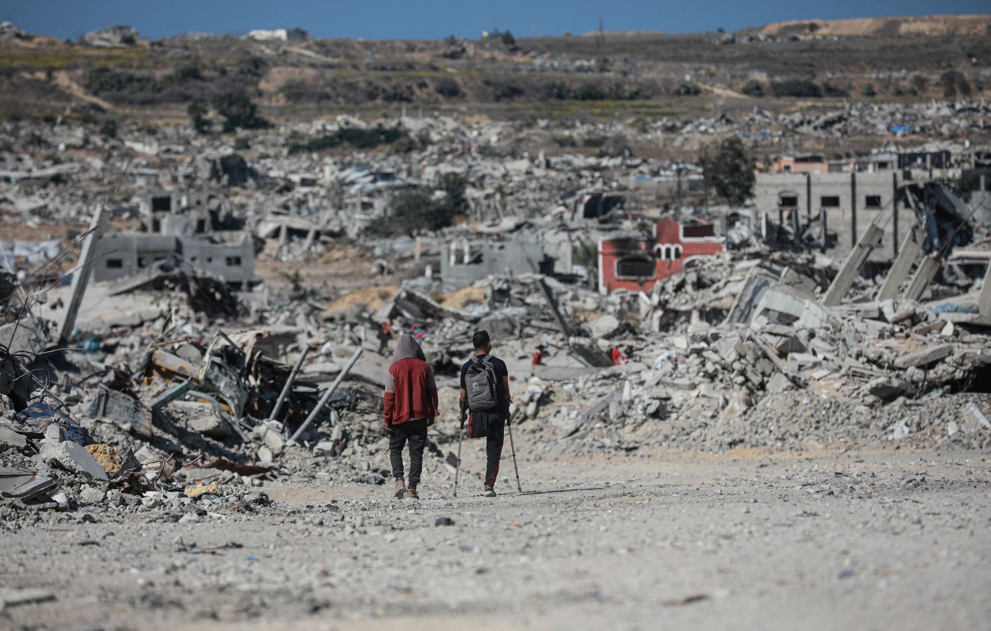 Deux personnes marchent dans un paysage de destruction, entourées de débris.