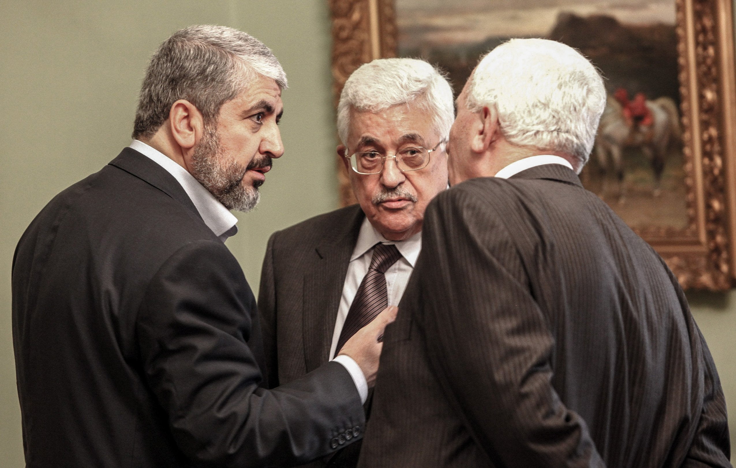 في الصورة، يظهر ثلاثة رجال يتبادلون الحديث في إطار رسمي. يرتدي الرجال بدلات رسمية، ويبدو عليهم التركيز أثناء المناقشة. خلفهم، يمكن رؤية لوحة فنية على الحائط تضيف لمسة ثقافية للمشهد. الجو العام يوحي بأن الحديث يجري حول موضوع مهم أو تفاوض سياسي.