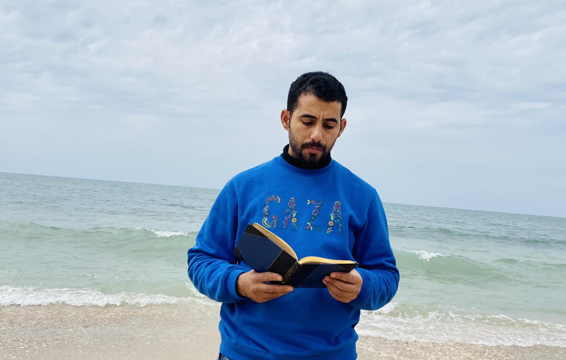 در این تصویر، مردی در کنار دریا ایستاده است و یک کتاب در دست دارد. او لباسی آبی رنگ به تن دارد که روی آن کلمه "GAZA" به چشم می‌خورد. پس‌زمینه تصویر را دریای آرام و آسمانی ابری تشکیل می‌دهد. موج‌های دریا به ساحل می‌رسند و فضای آرامی را به تصویر بخشیده‌اند. 
