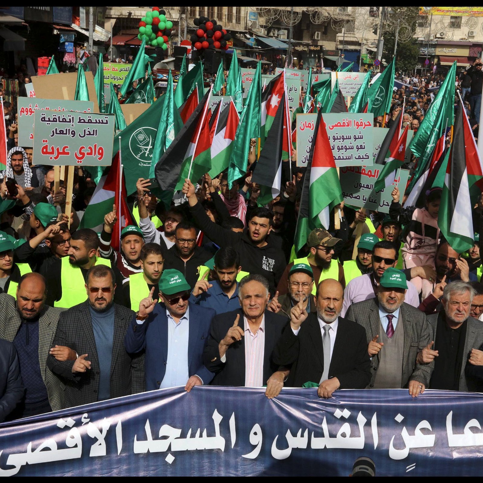 Manifestation avec drapeaux palestiniens, pancartes et participants en vert et noir.