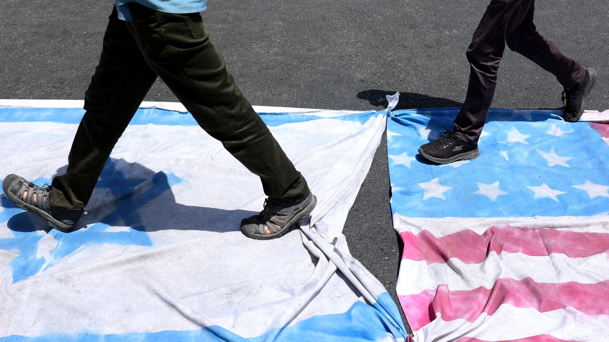 Deux personnes marchent sur des drapeaux américains et cubains étalés au sol.