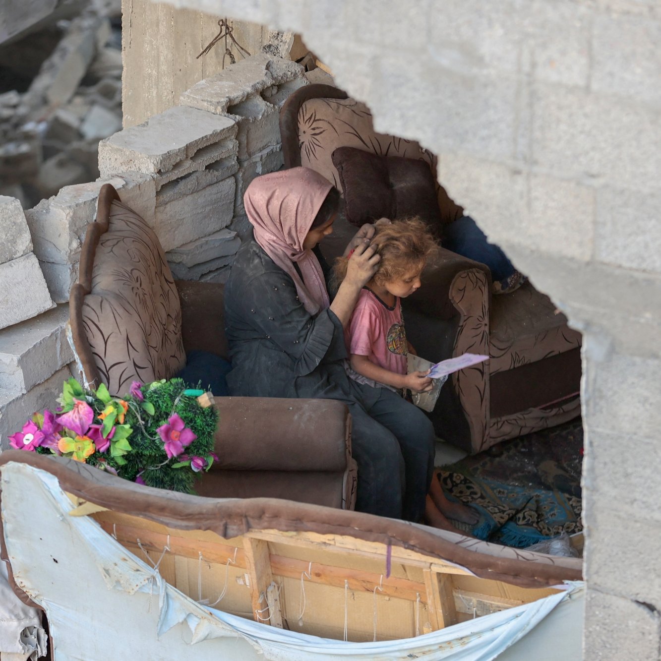 Une mère réconforte son enfant dans un espace endommagé, entourés de débris.