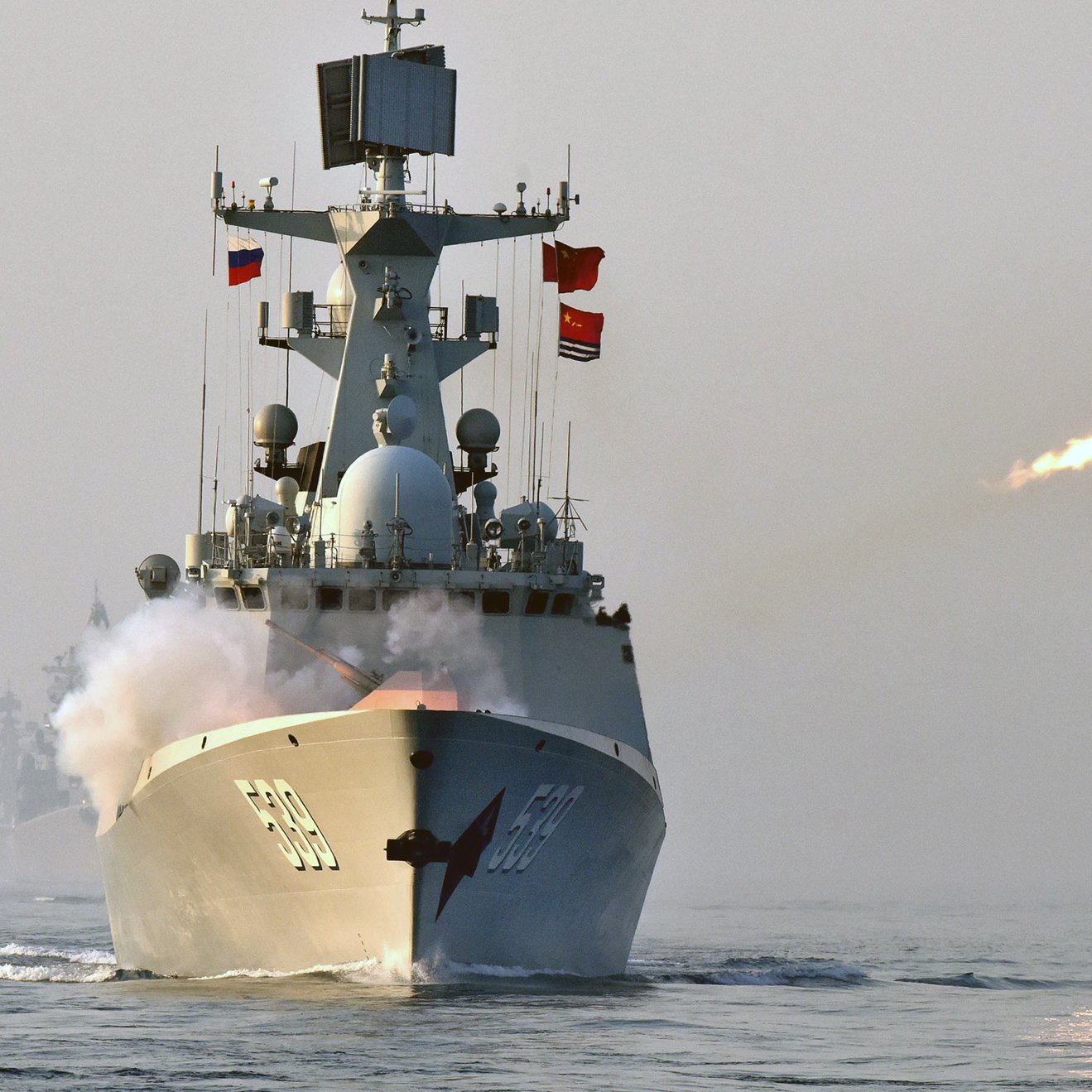 در تصویر یک ناو جنگی دیده می‌شود که در حال شلیک موشکی است. دود و آتش از بخش فوقانی ناو به سمت بالا می‌رود و موشک به سمت هدف پرتاب می‌شود. ناو دارای پرچم‌های مختلفی بر روی دکل‌های خود است که نشان‌دهنده حضور نیروی دریایی کشورها می‌باشد. دور تا دور ناو آب‌های دریا به صورت آرام دیده می‌شود و توده‌ای از مه در پس‌زمینه وجود دارد. این صحنه احتمالاً در حالت آماده‌باش یا تمرینات نظامی در حال وقوع است.