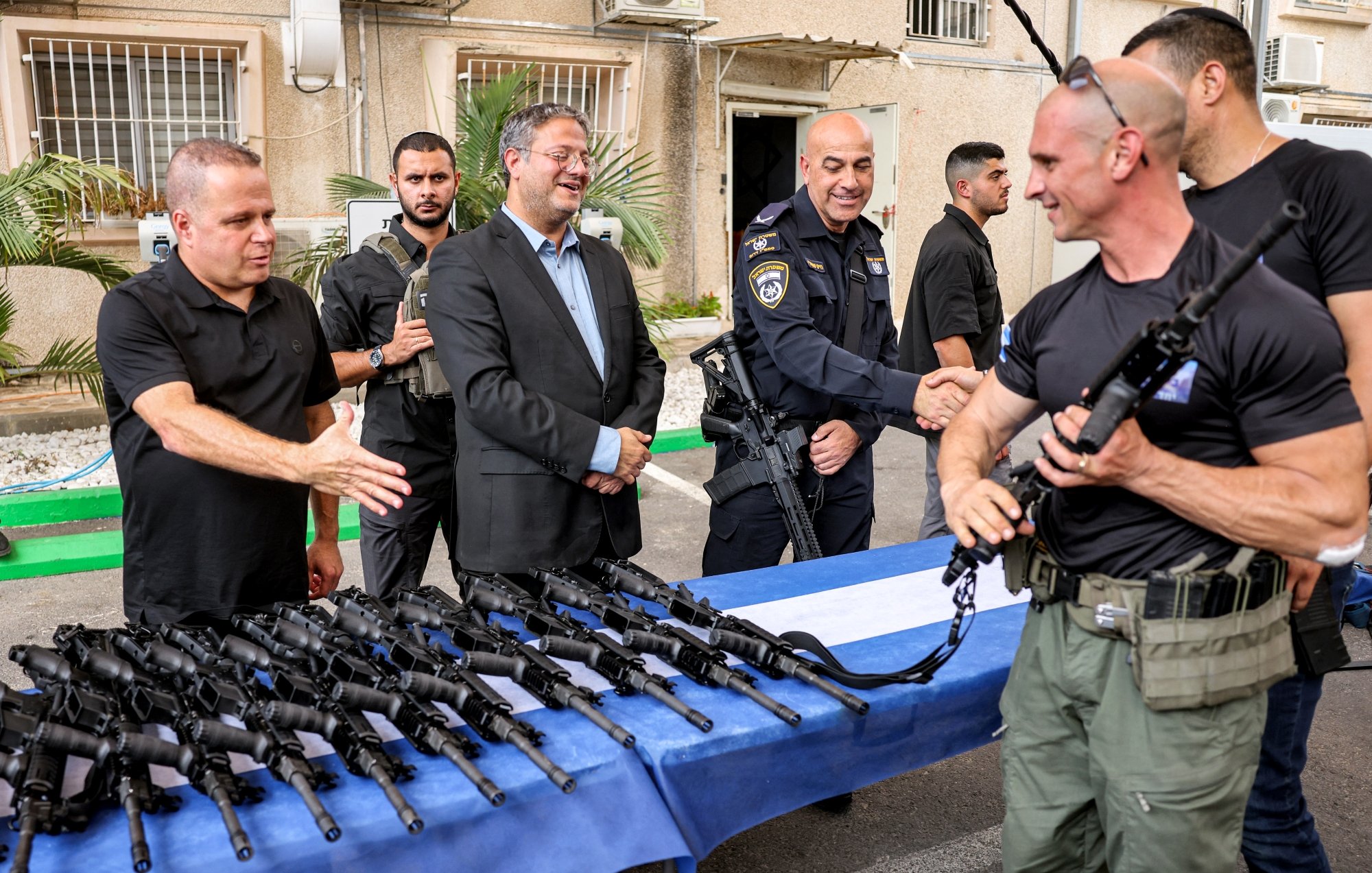 Des hommes en uniforme échangent des armes sur une table, sourires et discussions.