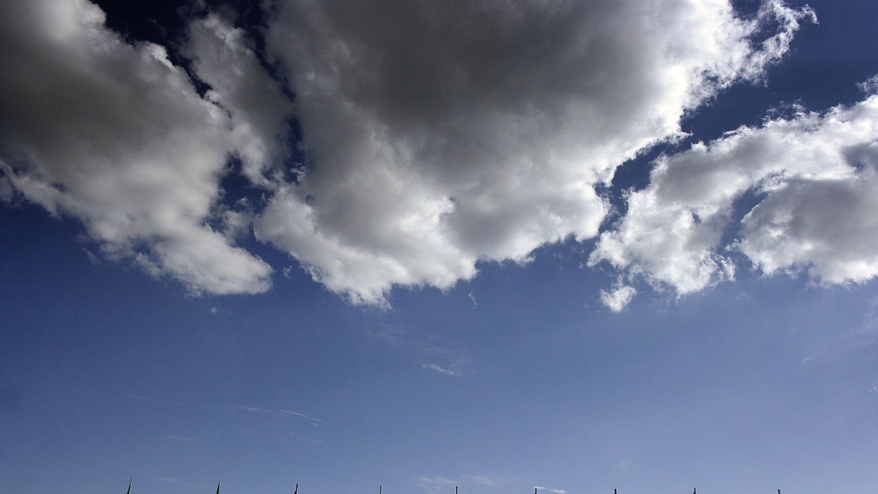 در این تصویر، چند پرچم در حال اهتزاز در برابر آسمانی آبی و ابری دیده می‌شود. پرچم‌ها به رنگ‌های سبز، سفید و قرمز هستند که رنگ‌های ملی ایران را نمایندگی می‌کنند. ابرهای سفید نیز در پس‌زمینه به زیبایی آسمان را تزئین کرده‌اند. این ترکیب تصویری از یک روز آفتابی و شاداب را به نمایش می‌گذارد.