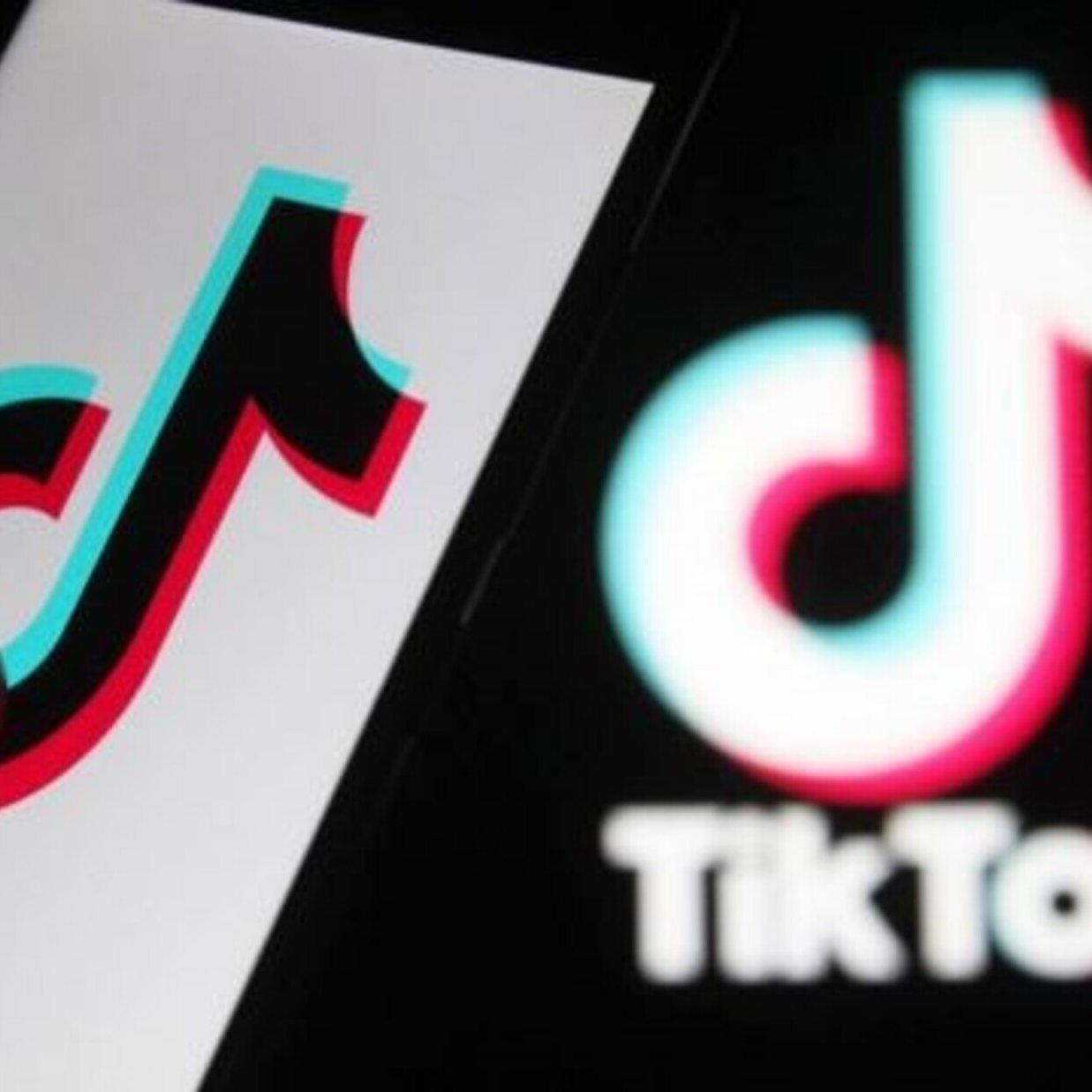 L'image montre un smartphone avec le logo de TikTok affiché à l'écran. On peut voir un doigt en train de toucher ou interagir avec le logo. À l'arrière-plan, il y a le logo de TikTok dans un style similaire, mais peut-être moins détaillé. Les couleurs principales du logo sont le noir, le rouge et le bleu, créant un effet visuel attrayant.