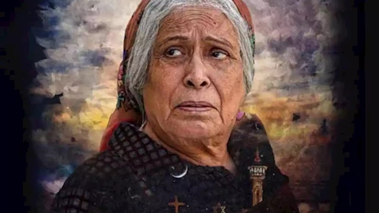 Cette image représente une femme âgée avec une expression pensive et préoccupée. Elle porte un foulard sur la tête et un vêtement sombre. En arrière-plan, on peut voir un paysage dramatique avec des nuages sombres et des silhouettes de bâtiments, évoquant peut-être un milieu rural ou historique. Le texte en bas de l'image semble être un titre ou un nom, mais il n'est pas identifiable sans plus de contexte. L'ensemble de la composition donne une impression d'émotion intense et de réflexion.