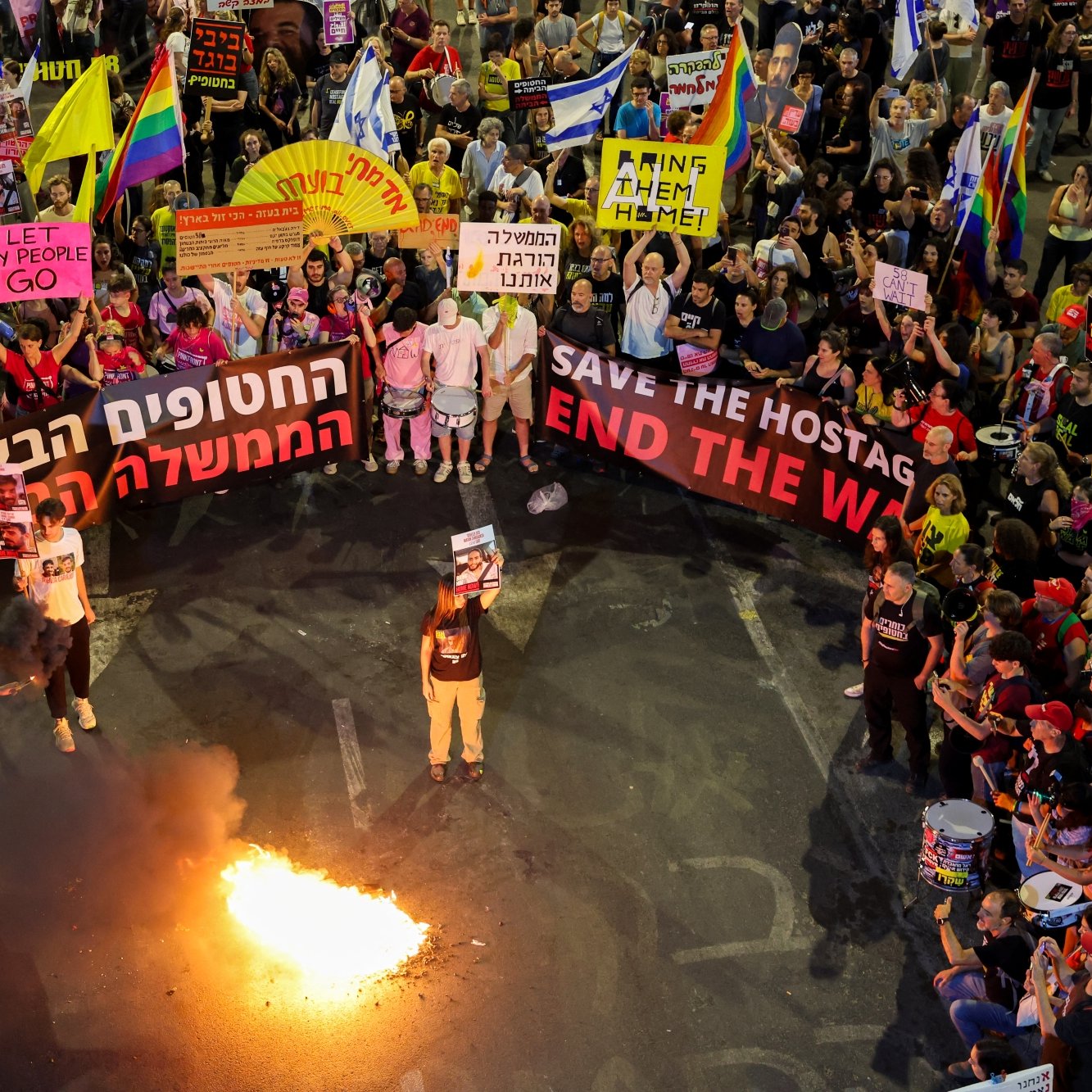 Manifestation animée avec des drapeaux et des pancartes, feu visible au centre.