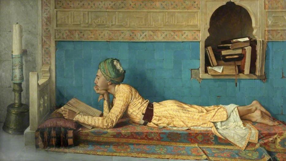 L'image représente un jeune homme allongé sur un tapis, plongé dans la lecture d'un livre. Il porte une tenue traditionnelle aux couleurs vives et un turban. L'arrière-plan est orné de motifs décoratifs et comprend une alcôve où sont disposés quelques livres. À gauche, une bougie sur un support éclaire la scène, créant une atmosphère calme et studieuse. L'ensemble évoque un moment de tranquillité et de contemplation.