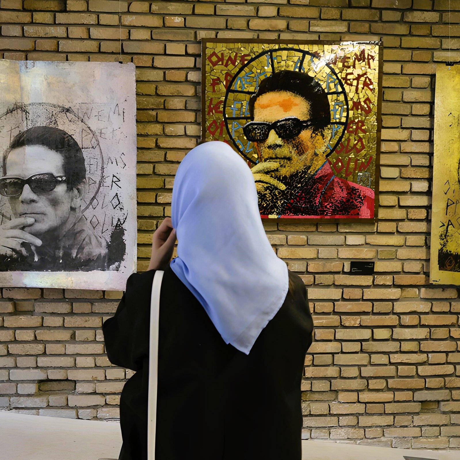 L'image montre une femme portant un hijab en train d'observer des œuvres d'art accrochées à un mur en briques. Les tableaux représentent un homme avec des lunettes de soleil, entouré de motifs et de couleurs variés. L'ambiance semble artistique et contemporaine, avec un jeu de lumière qui attire l'œil vers les œuvres.