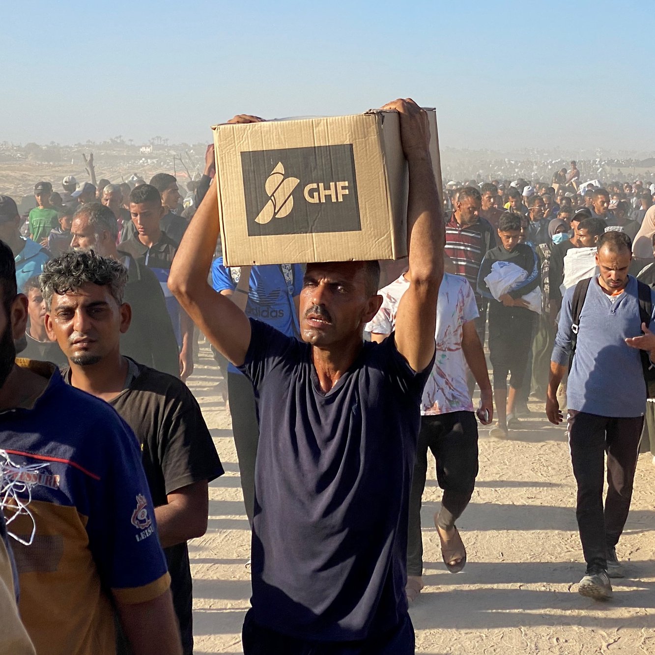 Un groupe de personnes marchent, portant des cartons dans un environnement poussiéreux.