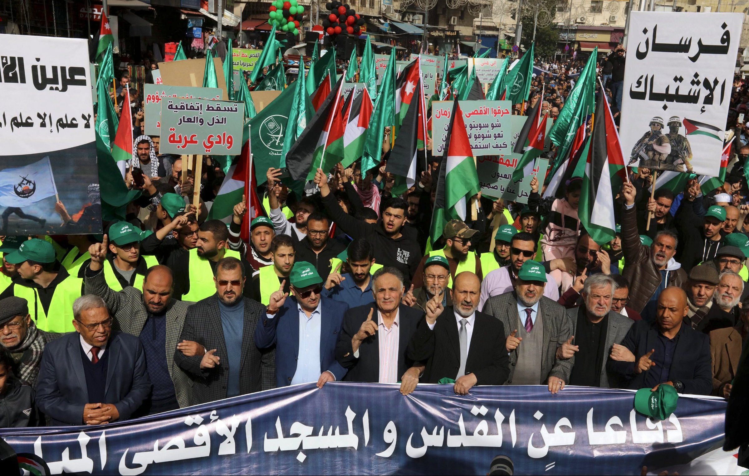 Manifestation avec drapeaux palestiniens, pancartes et participants en vert et noir.