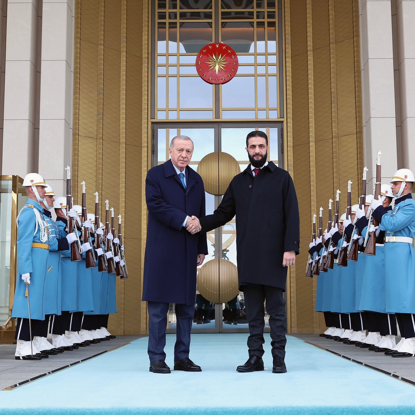 الصورة تُظهر شخصين يتصافحان أمام مدخل فخم، حيث يقف الجنود في الخلفية في تنسيق دقيق. الأجواء رسمية وتعكس حدثاً مهماً.