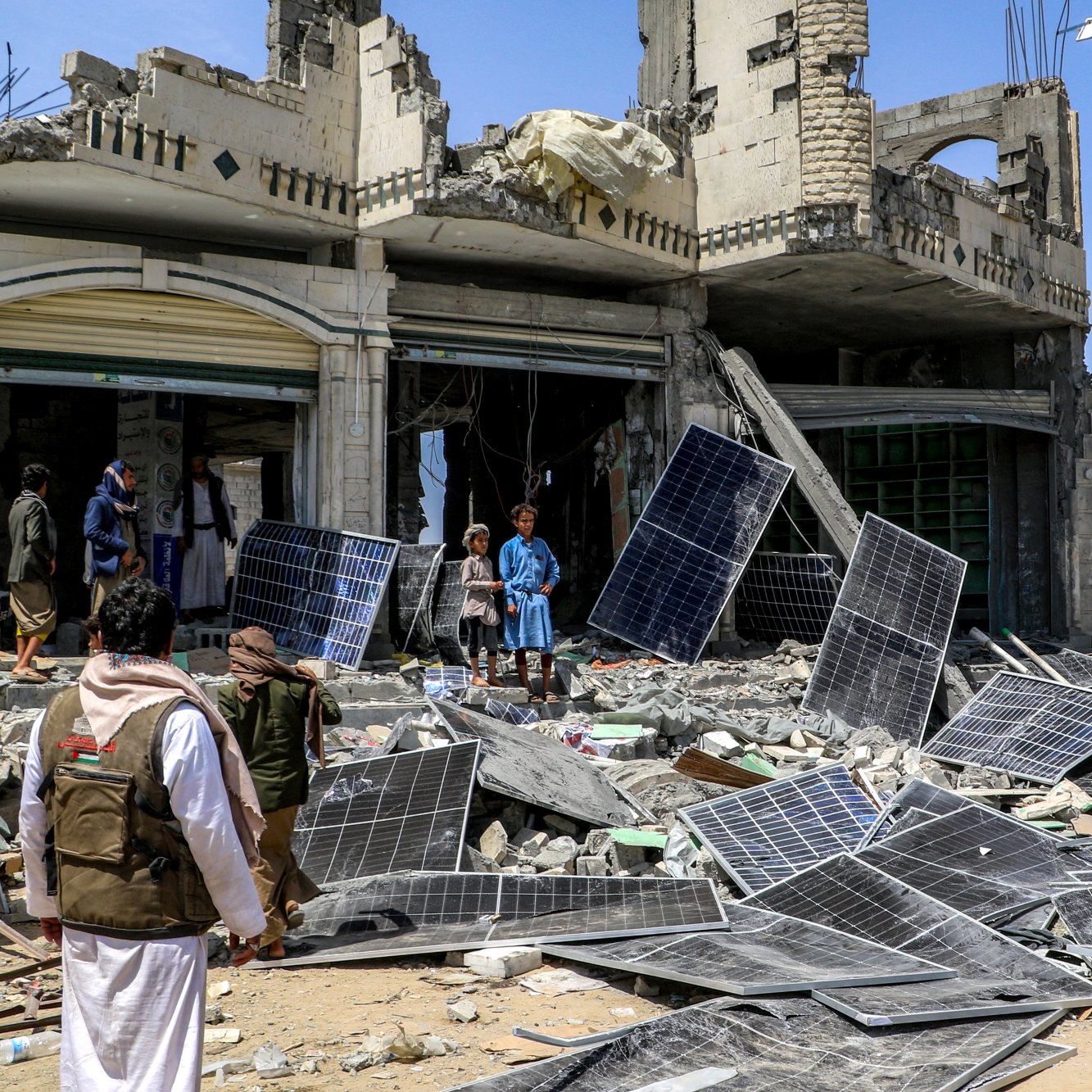 Destruction : bâtiment effondré, débris et panneaux solaires éparpillés autour.