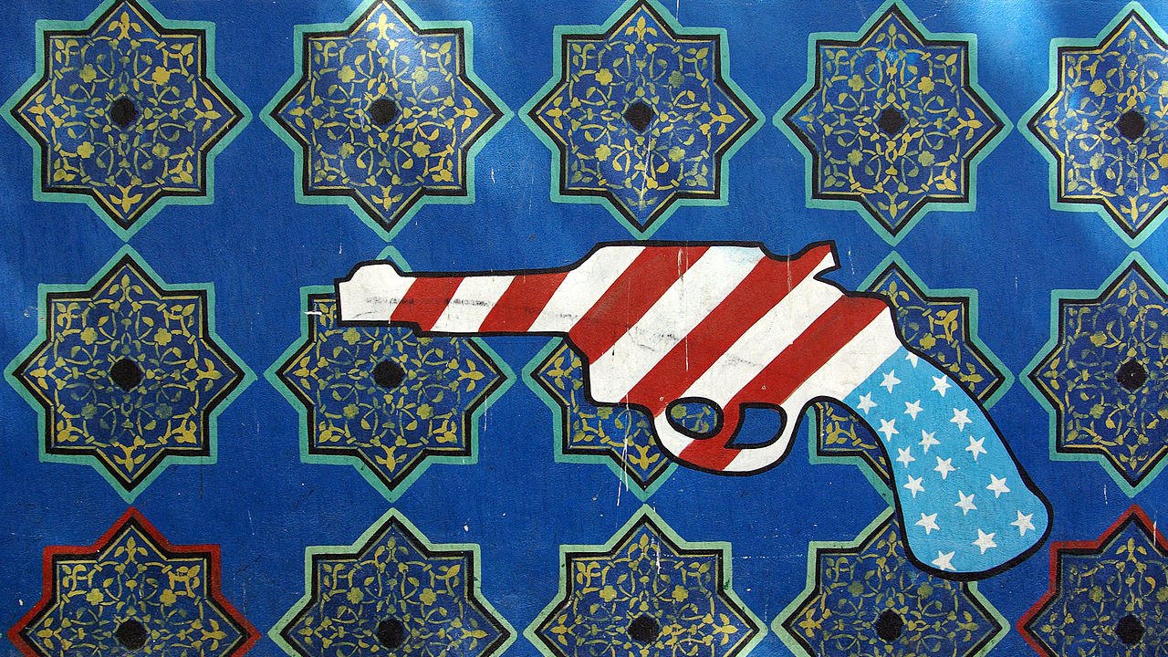 این تصویر شامل یک زمینه آبی با الگوهای هندسی و طراحی‌های سنتی است که به رنگ‌های طلایی و سبز نمایان شده‌اند. در وسط تصویر، یک نقاشی از یک تفنگ نمایش داده شده که با رنگ‌های پرچم ایالات متحده، یعنی سرخ، سفید و آبی، تزئین شده است. طراحی تفنگ با الگوهای زمینه تضاد دارد و به نوعی تأملی از الهام غربی در هنر ایرانی را به تصویر می‌کشد.