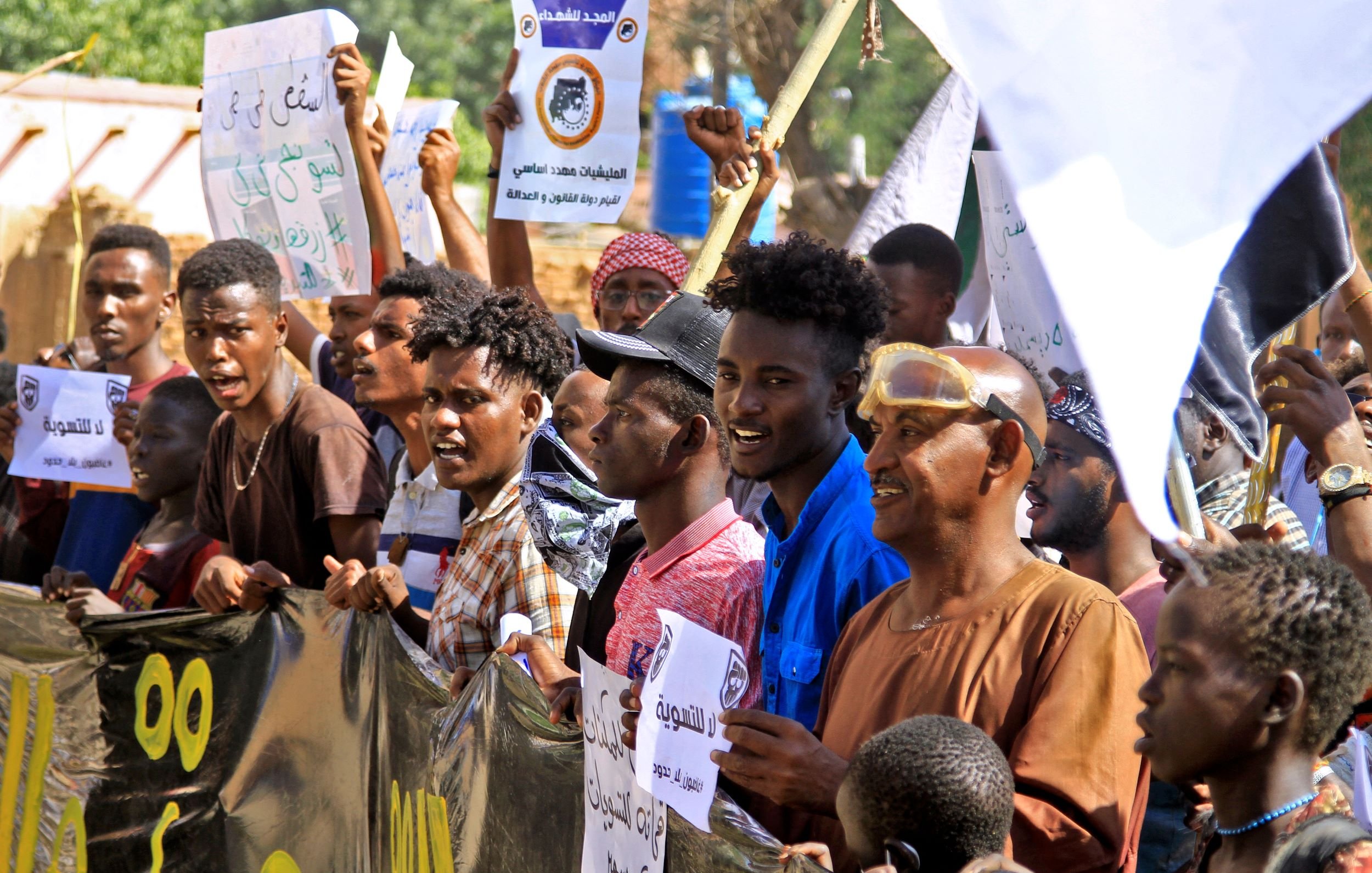 در این تصویر گروهی از مردم در حال برگزاری تجمع یا تظاهرات هستند. آن‌ها پلاکاردهایی در دست دارند که روی آن‌ها نوشته‌هایی به زبان عربی وجود دارد. به نظر می‌رسد که این جمعیت شامل مردان جوان و بزرگسال است که برخی از آن‌ها لباس‌های سنتی و برخی لباس‌های عادی پوشیده‌اند. فضای تصویر نشان‌دهنده شور و هیجان جمعیت است و احتمالا این تظاهرات به یک مسئله اجتماعی یا سیاسی مرتبط است.