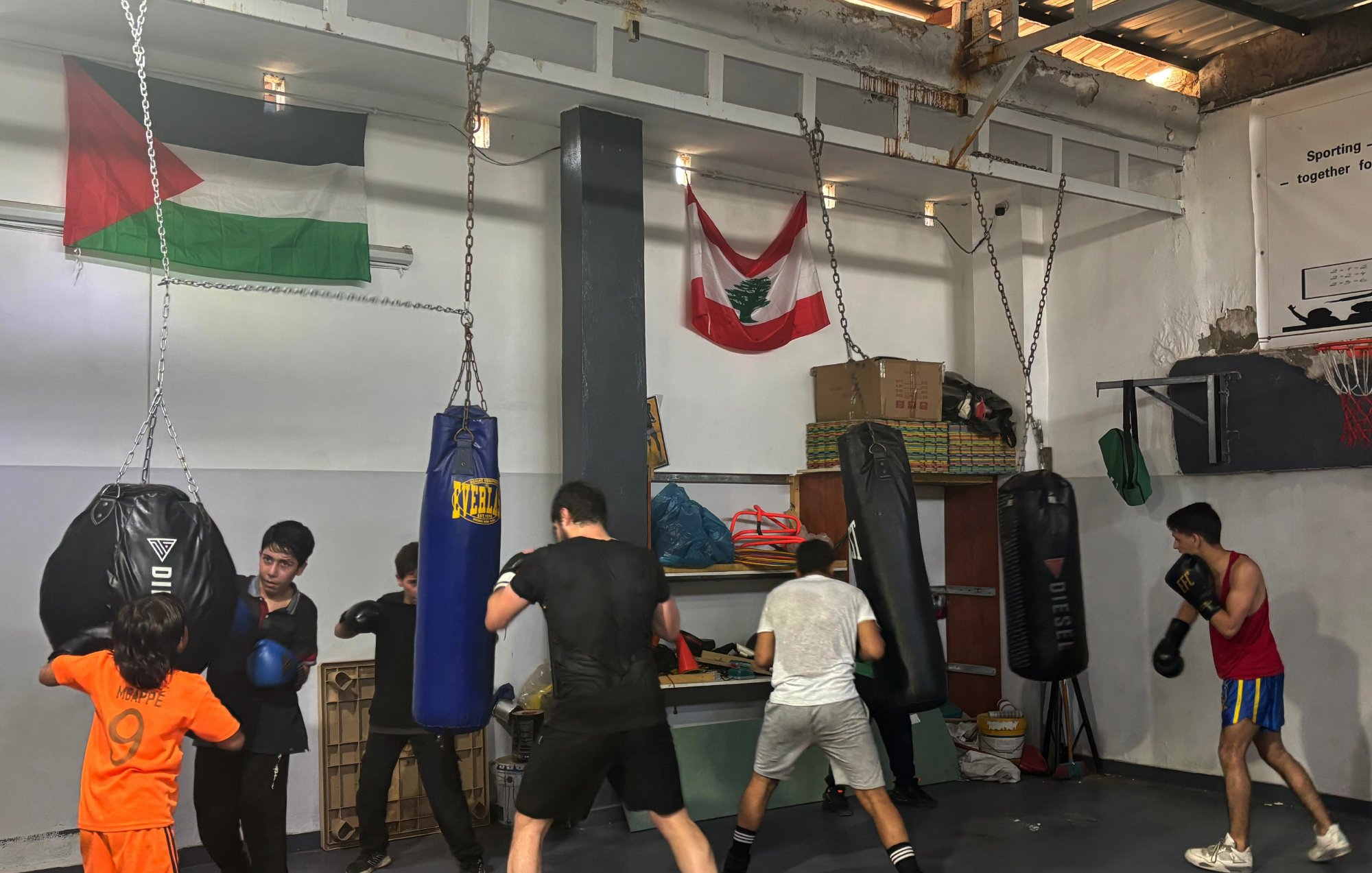 مجموعة من الشباب يتدربون في قاعة ملاكمة، تتدلى أكياس الملاكمة من السقف.
