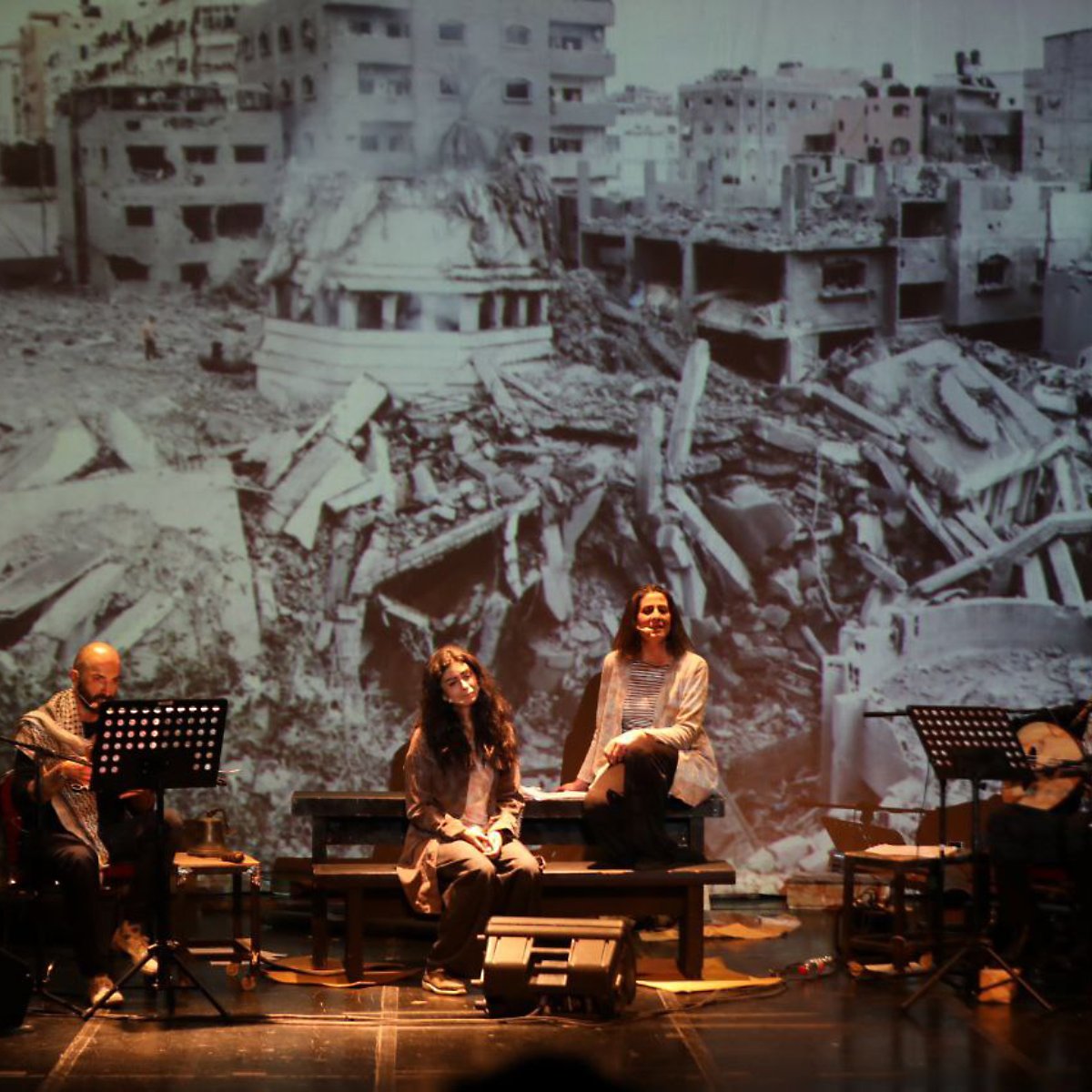 Quatre artistes sur scène, avec une projection d'un paysage de destruction en arrière-plan.